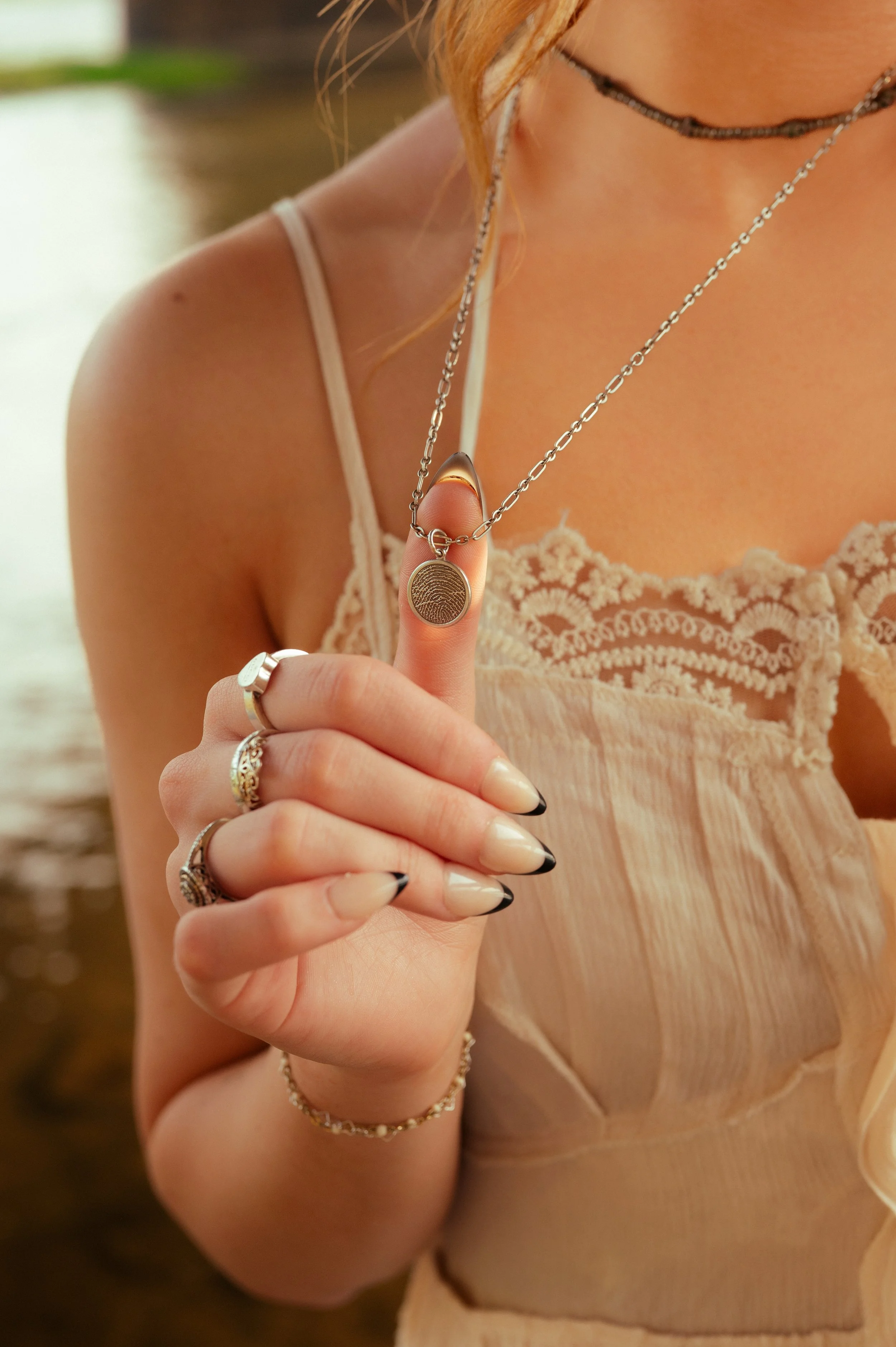 A close-up of layered rings and a pendant necklace at the river