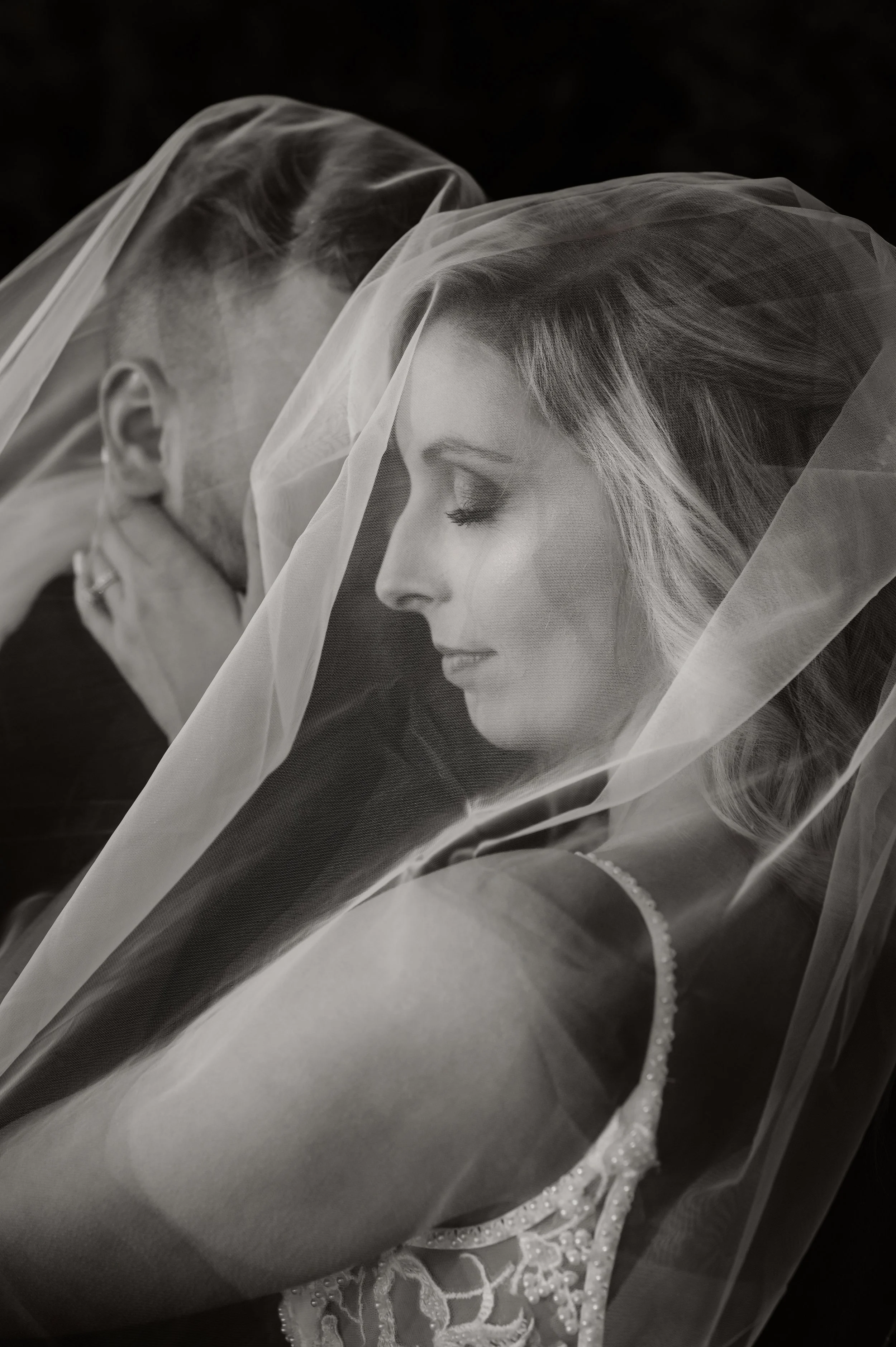 Bride and groom wrapped together under her veil in a black-and-white portrait