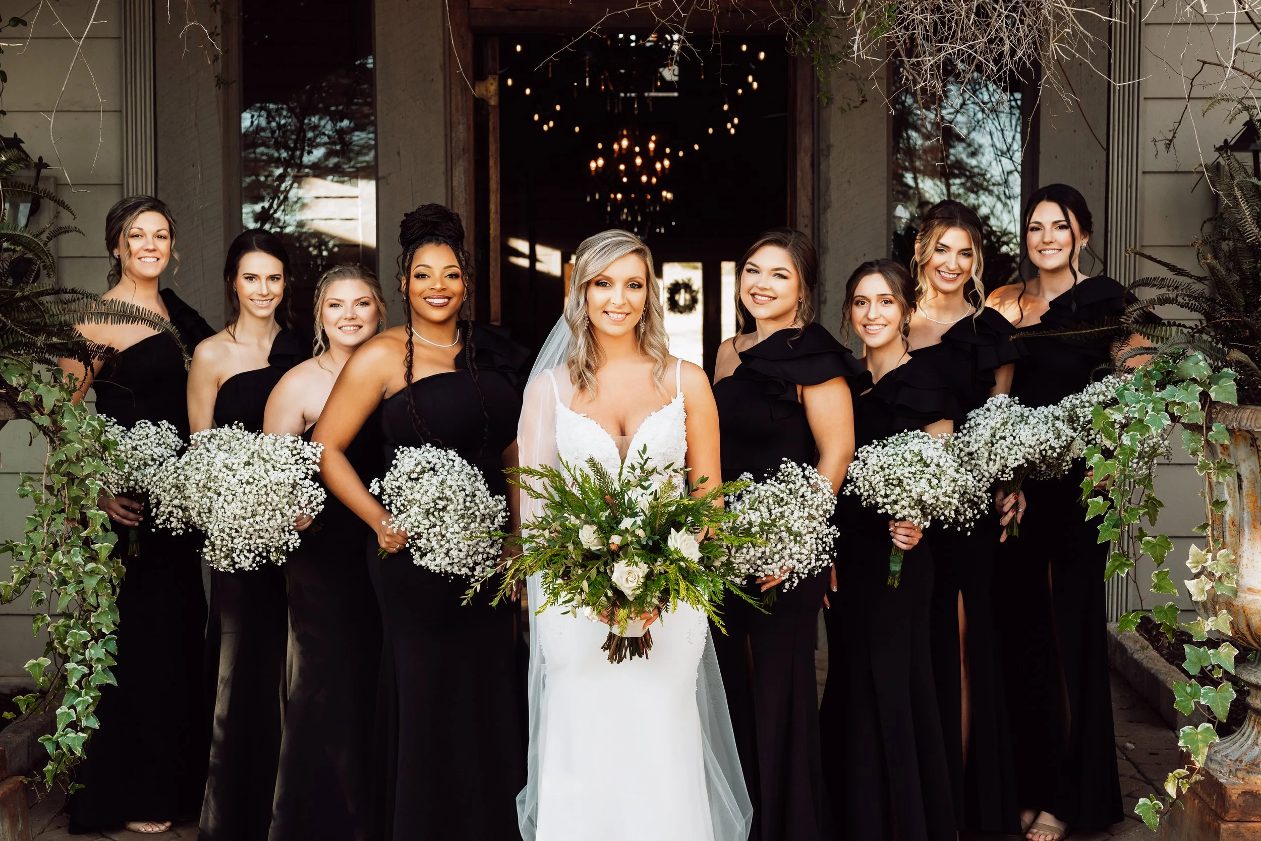 Bride surrounded by her bridesmaids in black gowns, all holding baby's-breath bouquets