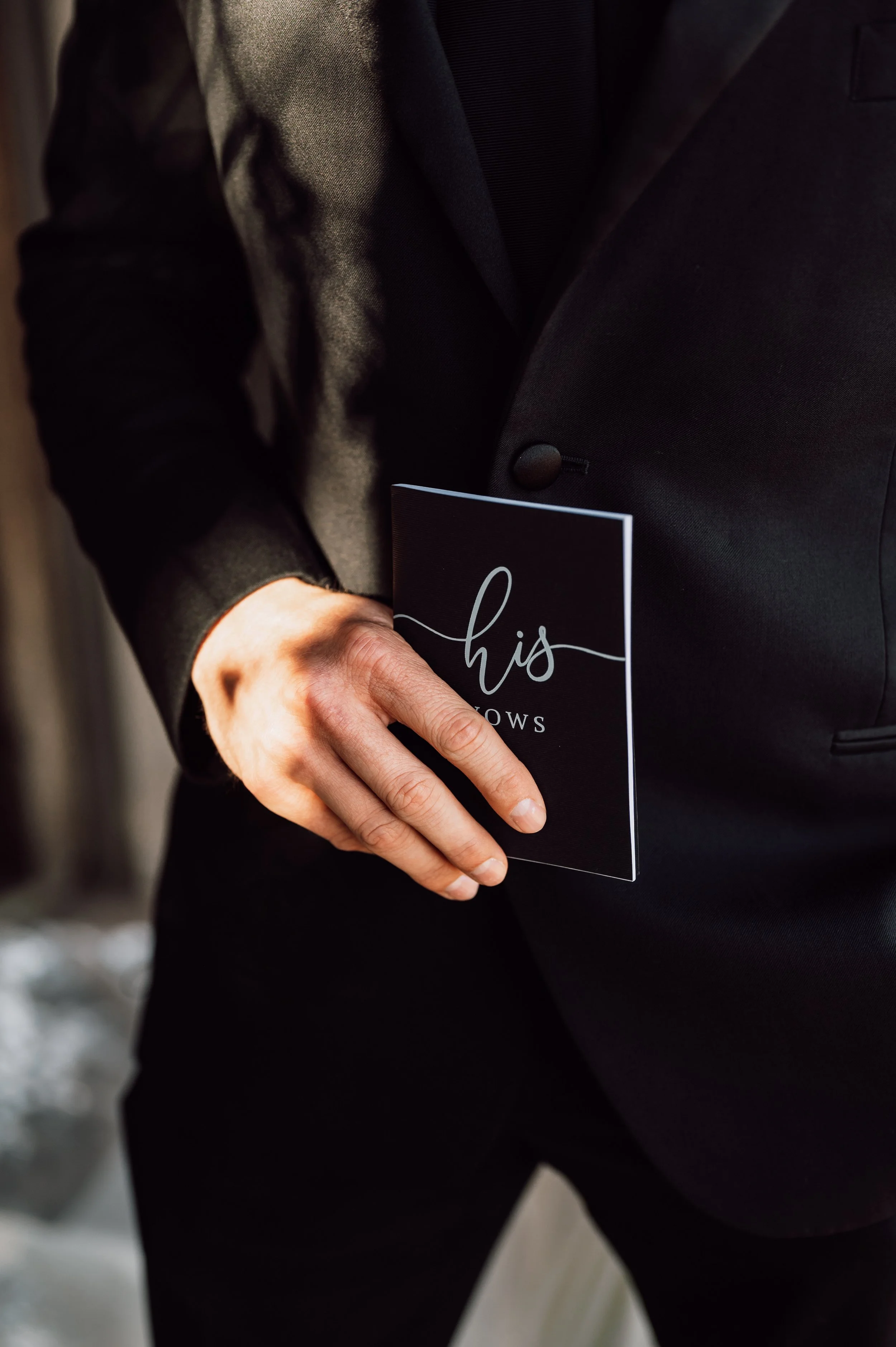 Groom in a black tuxedo holding his vow book before the ceremony