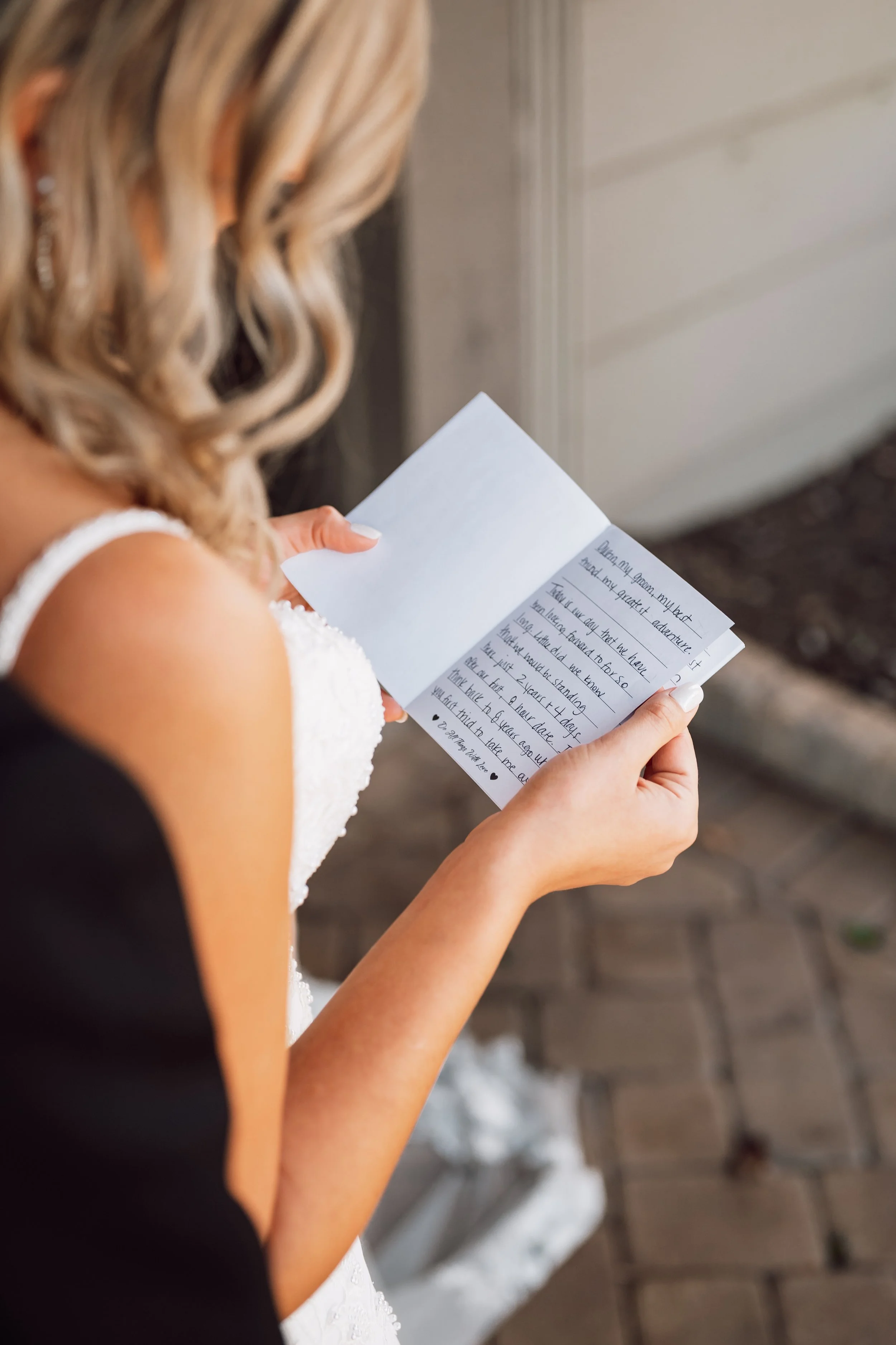 The bride reading her handwritten vows, head down, in a black-strapped gown