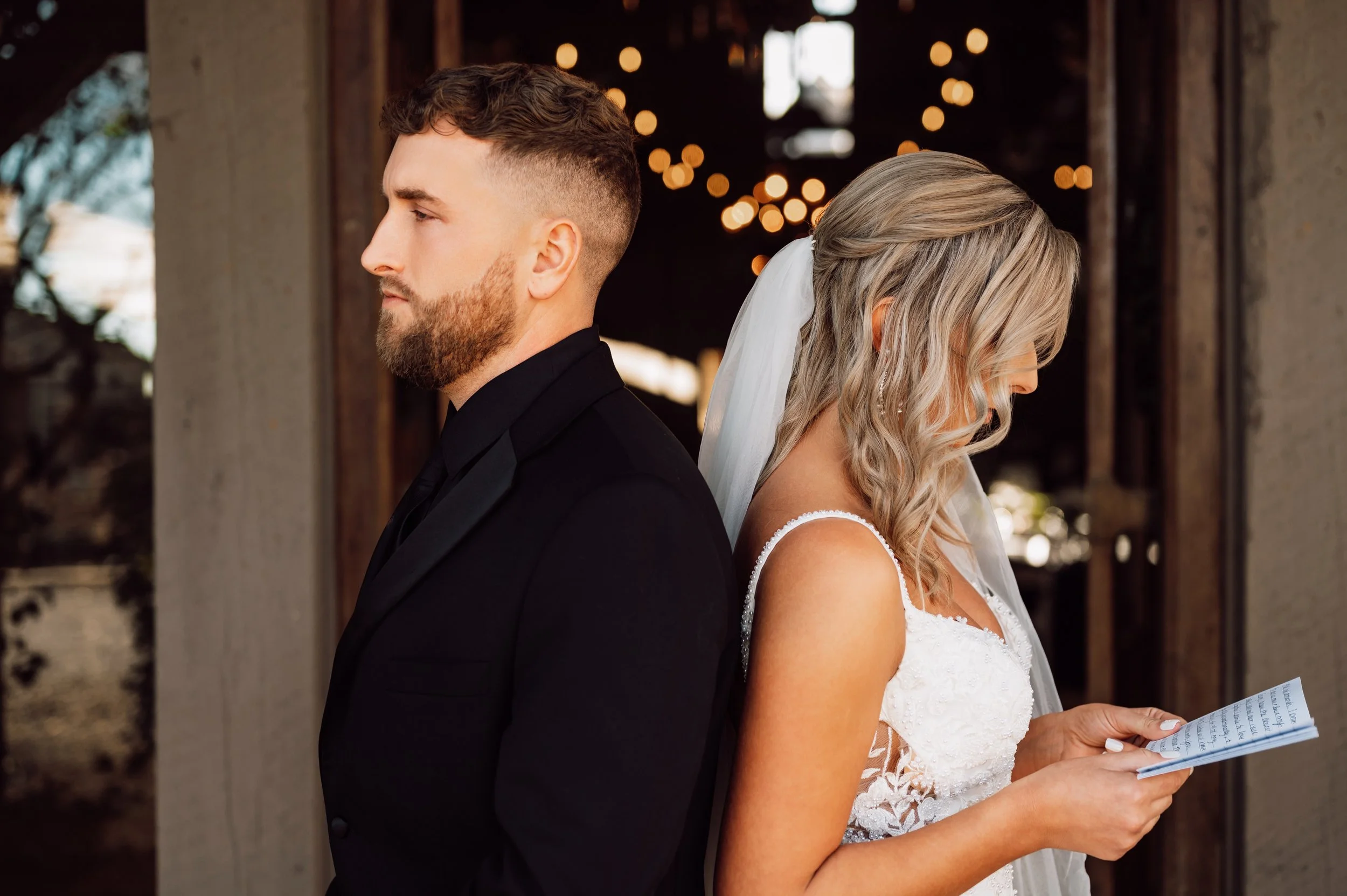 Bride and groom standing back to back before their first look, the bride reading a handwritten letter