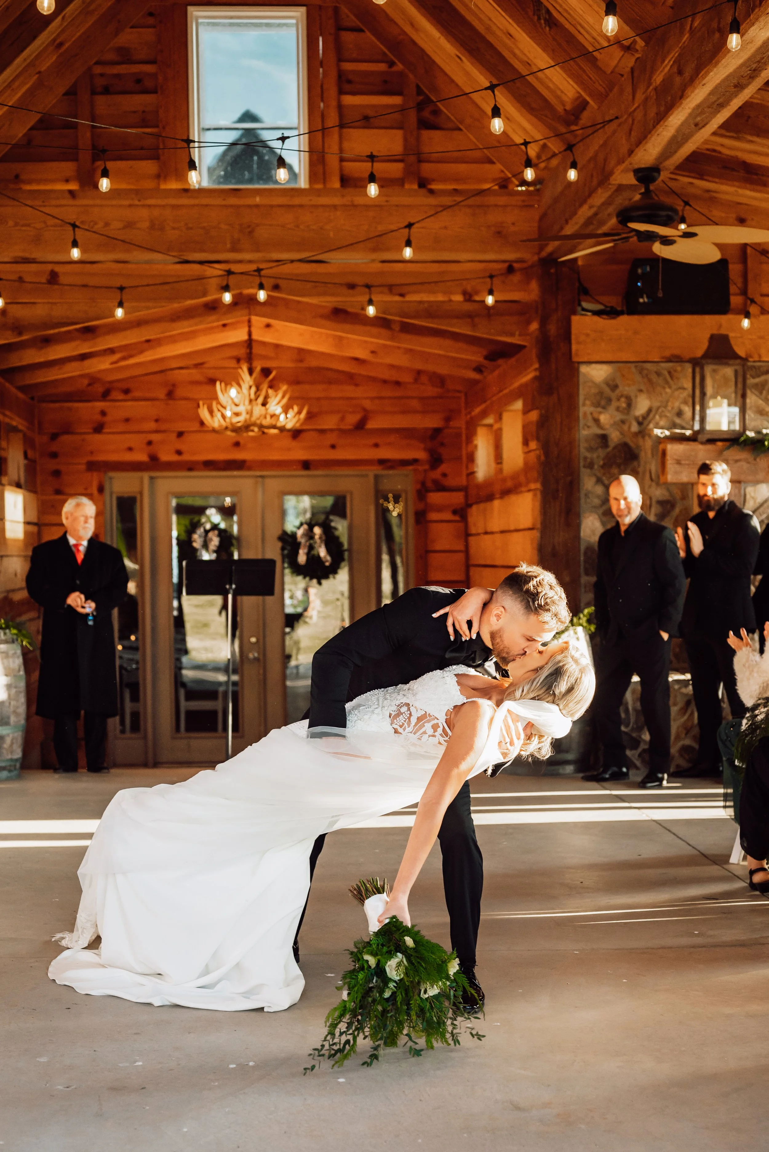 Groom dipping the bride for a kiss in a timber pavilion strung with lights
