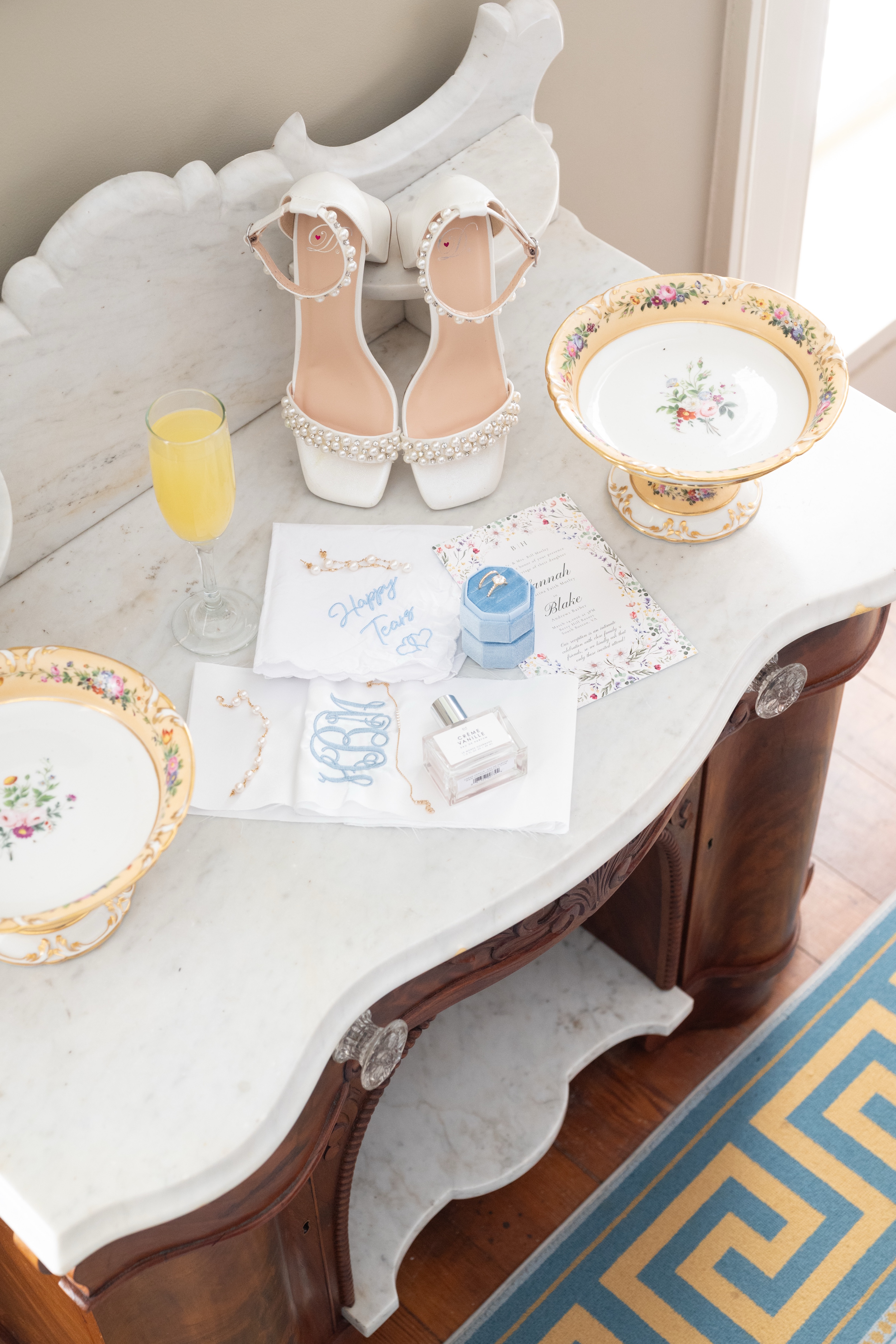 Pearl-strapped bridal heels, the invitation suite, perfume and a mimosa arranged on a marble dresser