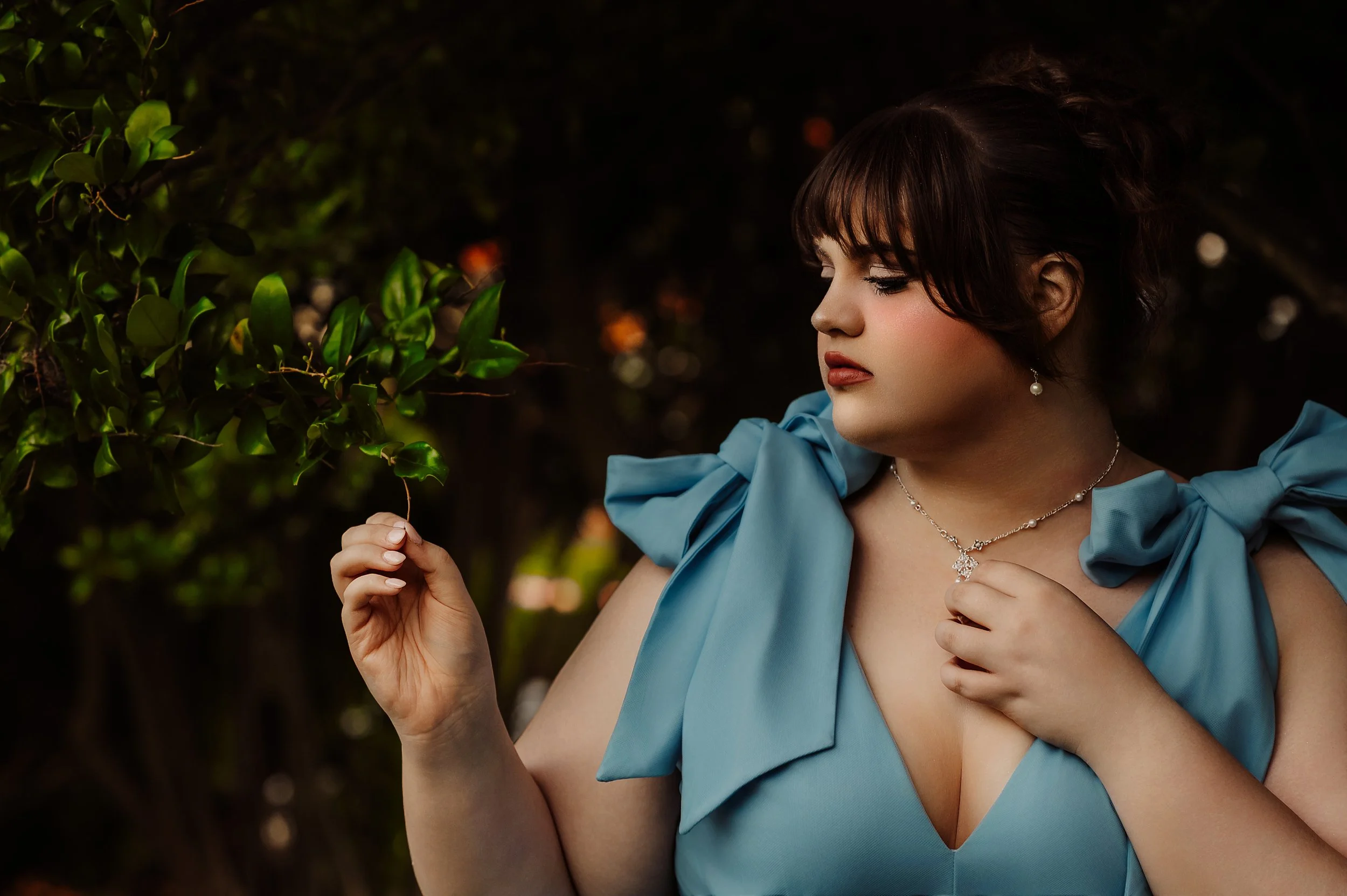 A senior in a powder-blue bow-shoulder gown beside a garden hedge