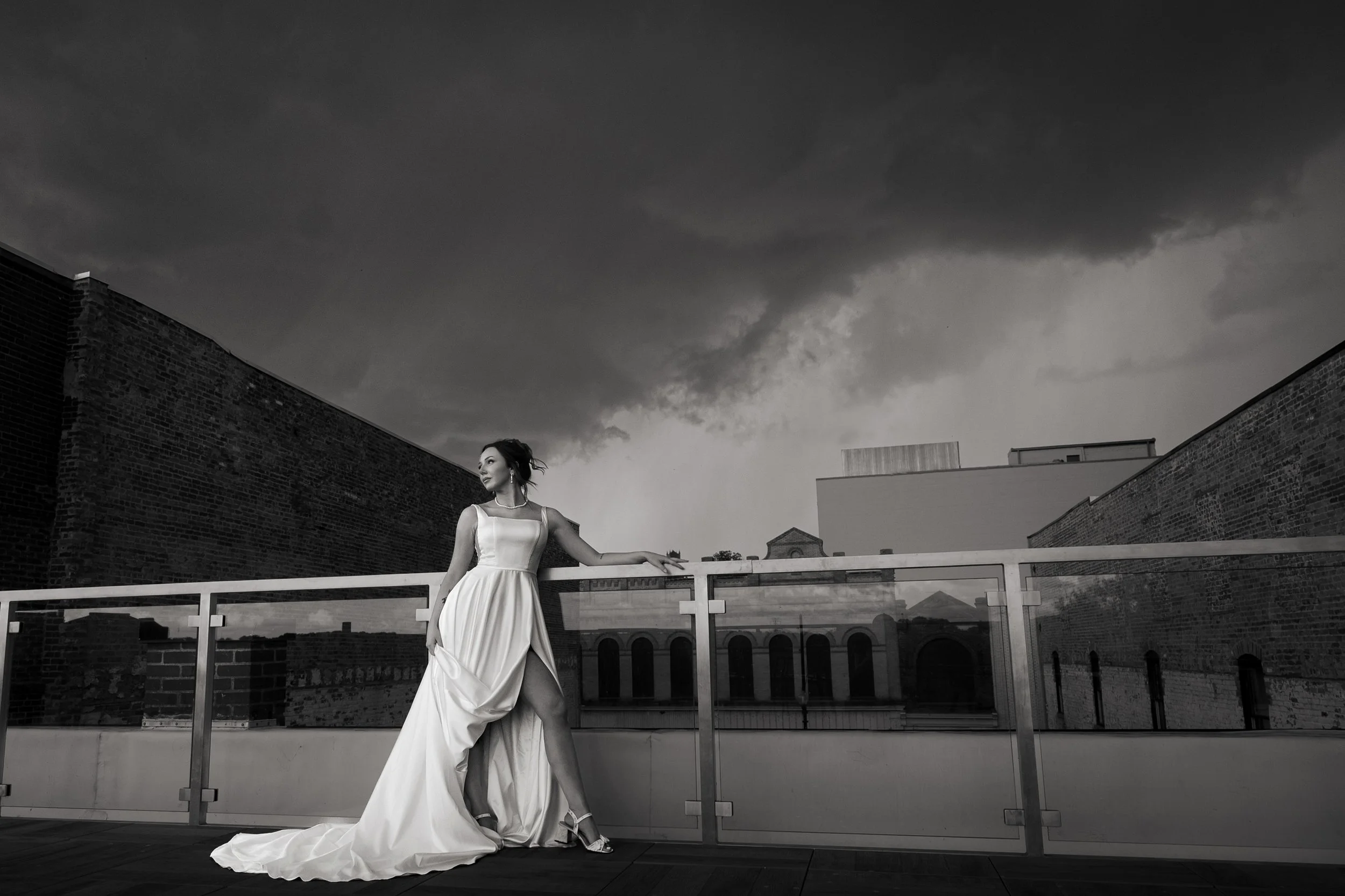 Bride on a downtown rooftop beneath a dramatic storm sky, brick warehouses behind her
