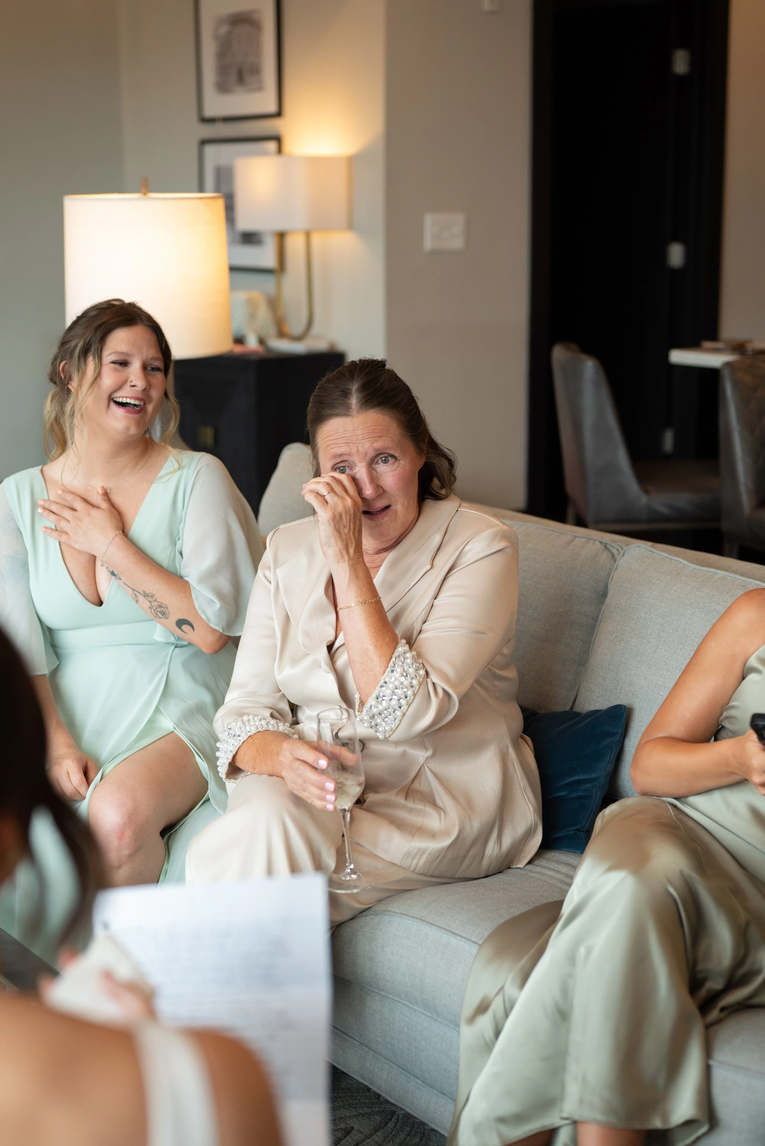 Mother of the bride tearing up on the couch as the bride reads a letter aloud