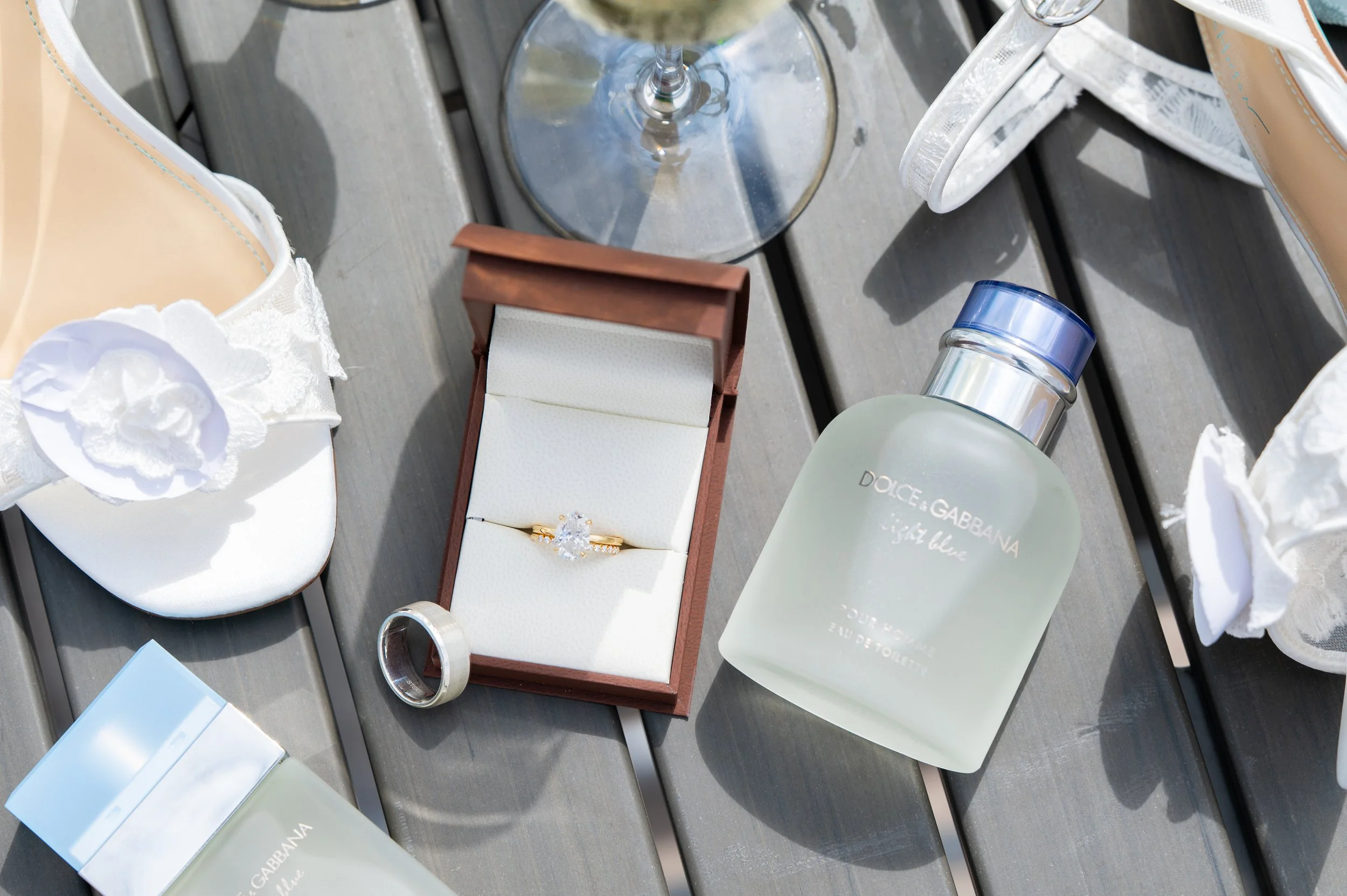 Detail flat lay of the wedding rings, bridal shoes, perfume, and champagne
