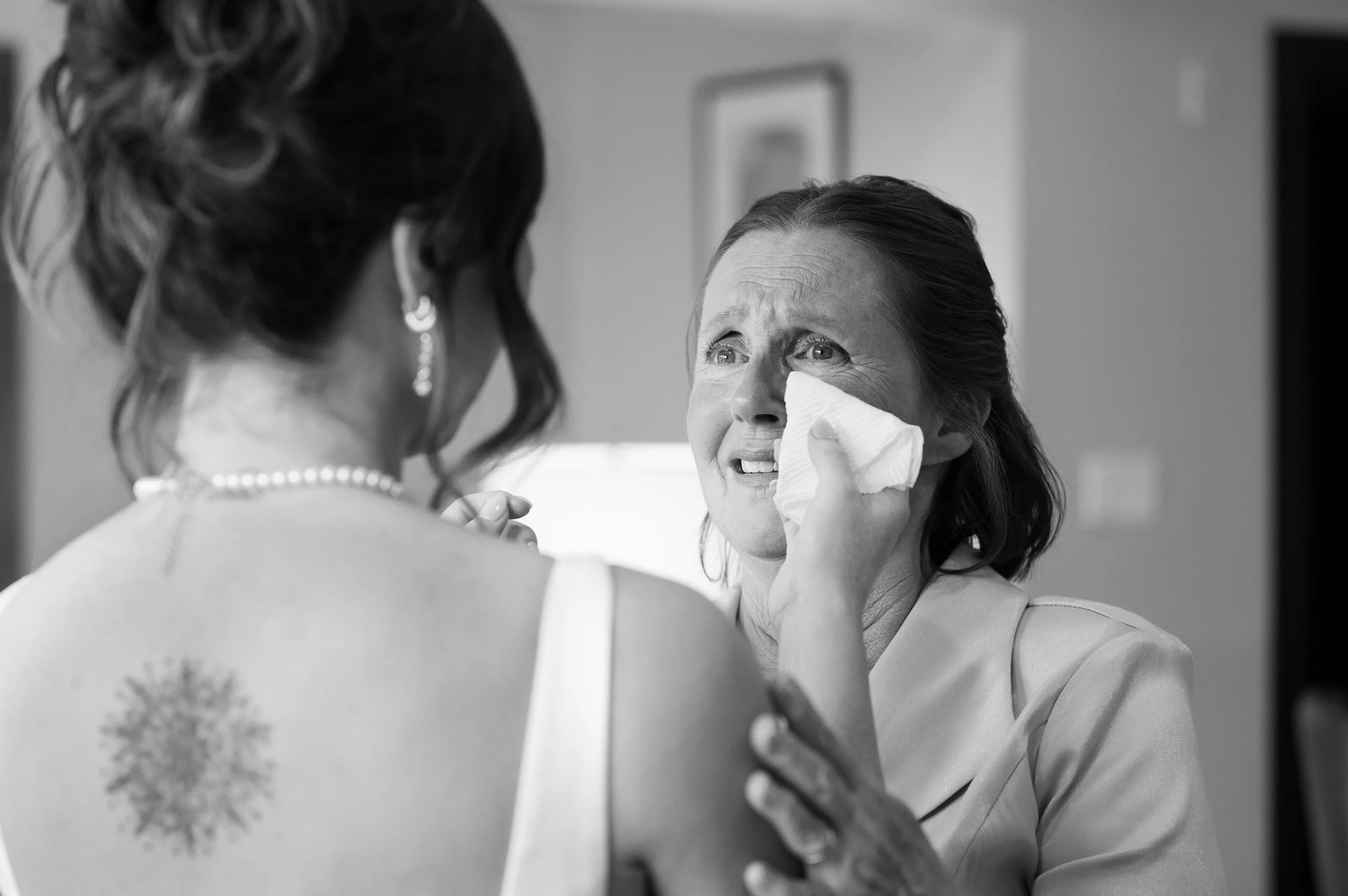 Mother of the bride wiping away happy tears while the bride finishes getting ready