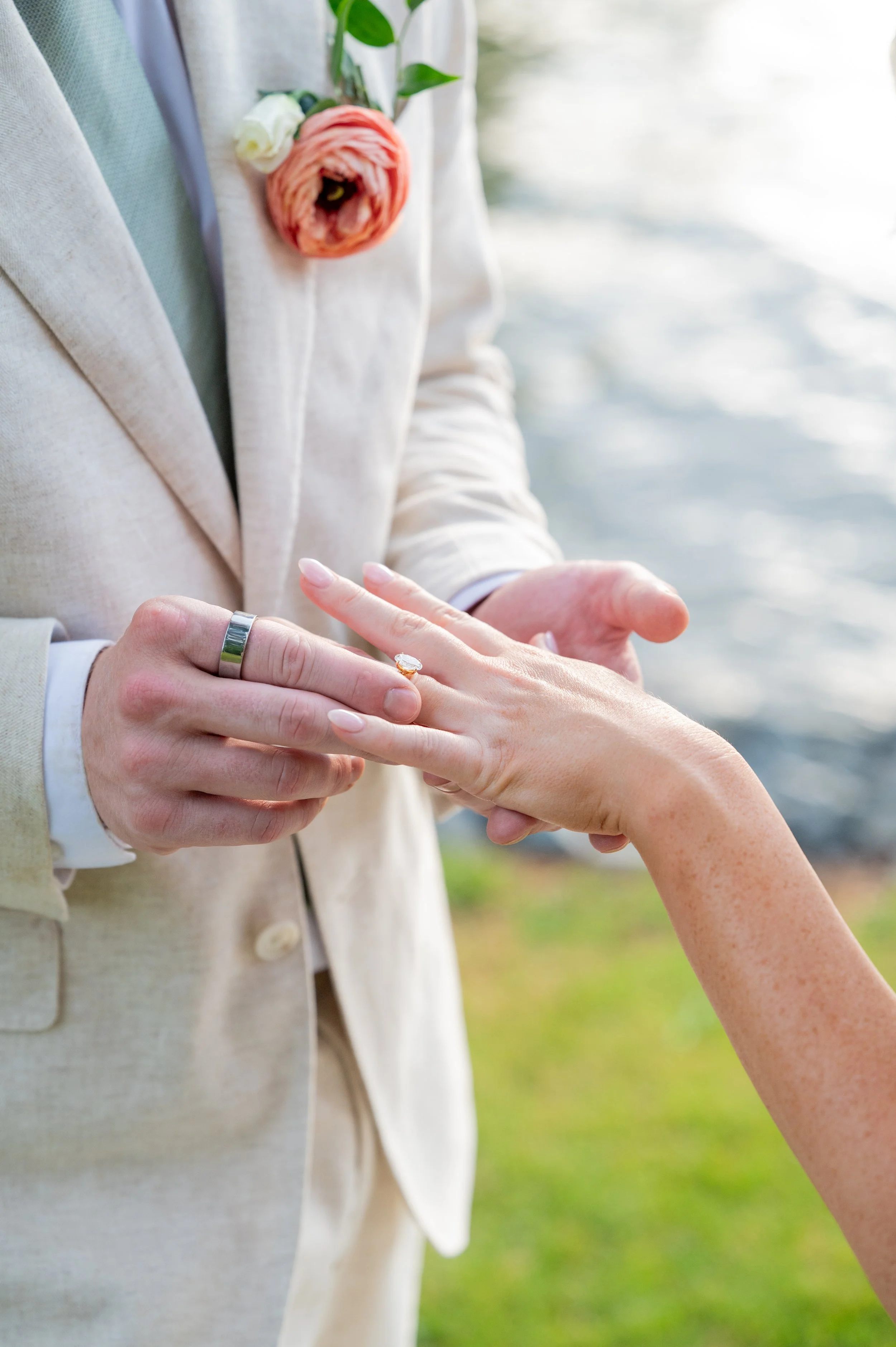 Groom sliding the ring onto the bride's finger at a lakeside ceremony