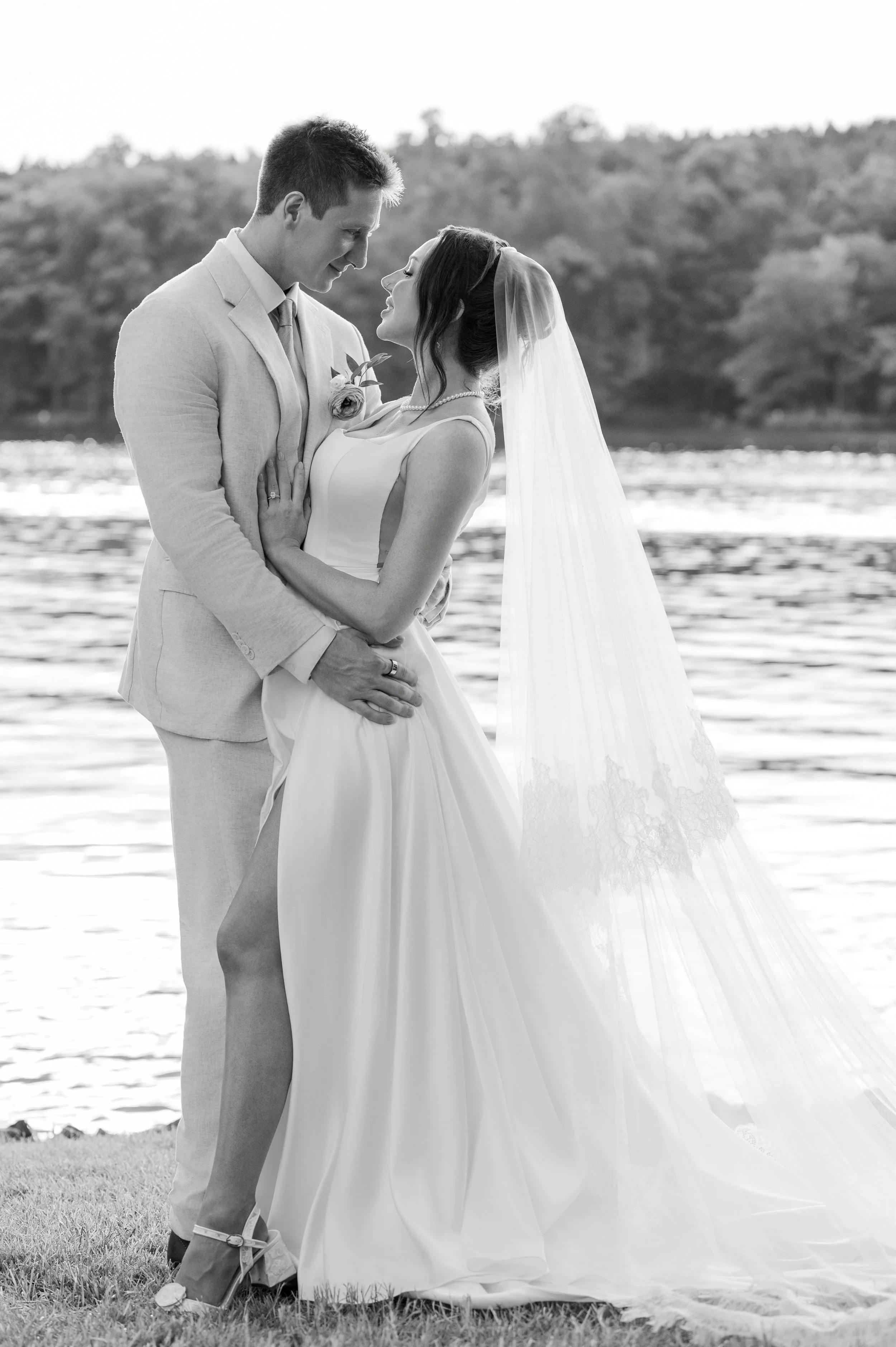Bride and groom nose to nose at the water's edge, her long veil trailing