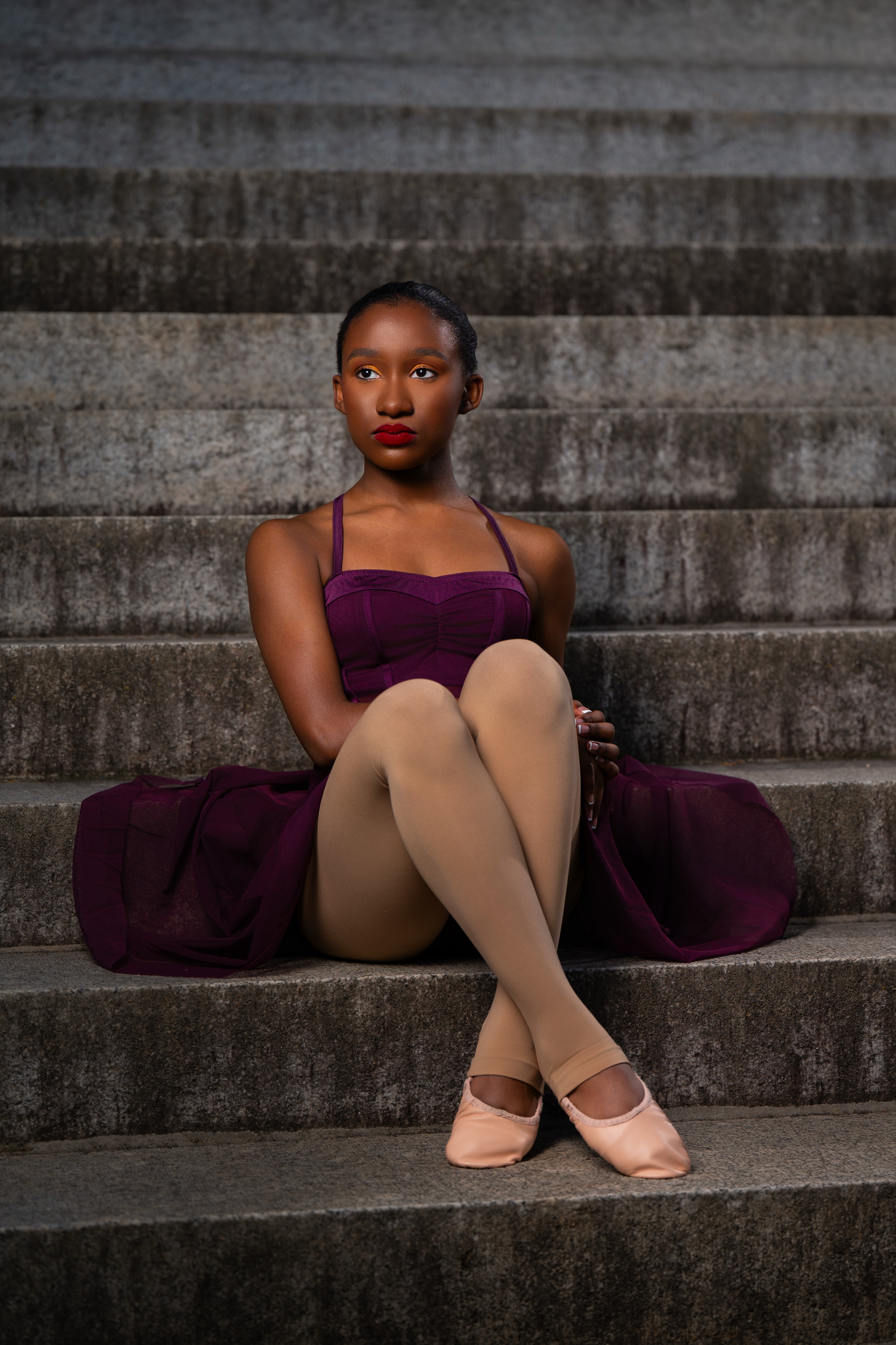 Dancer in a plum leotard and pointe shoes seated on weathered concrete steps