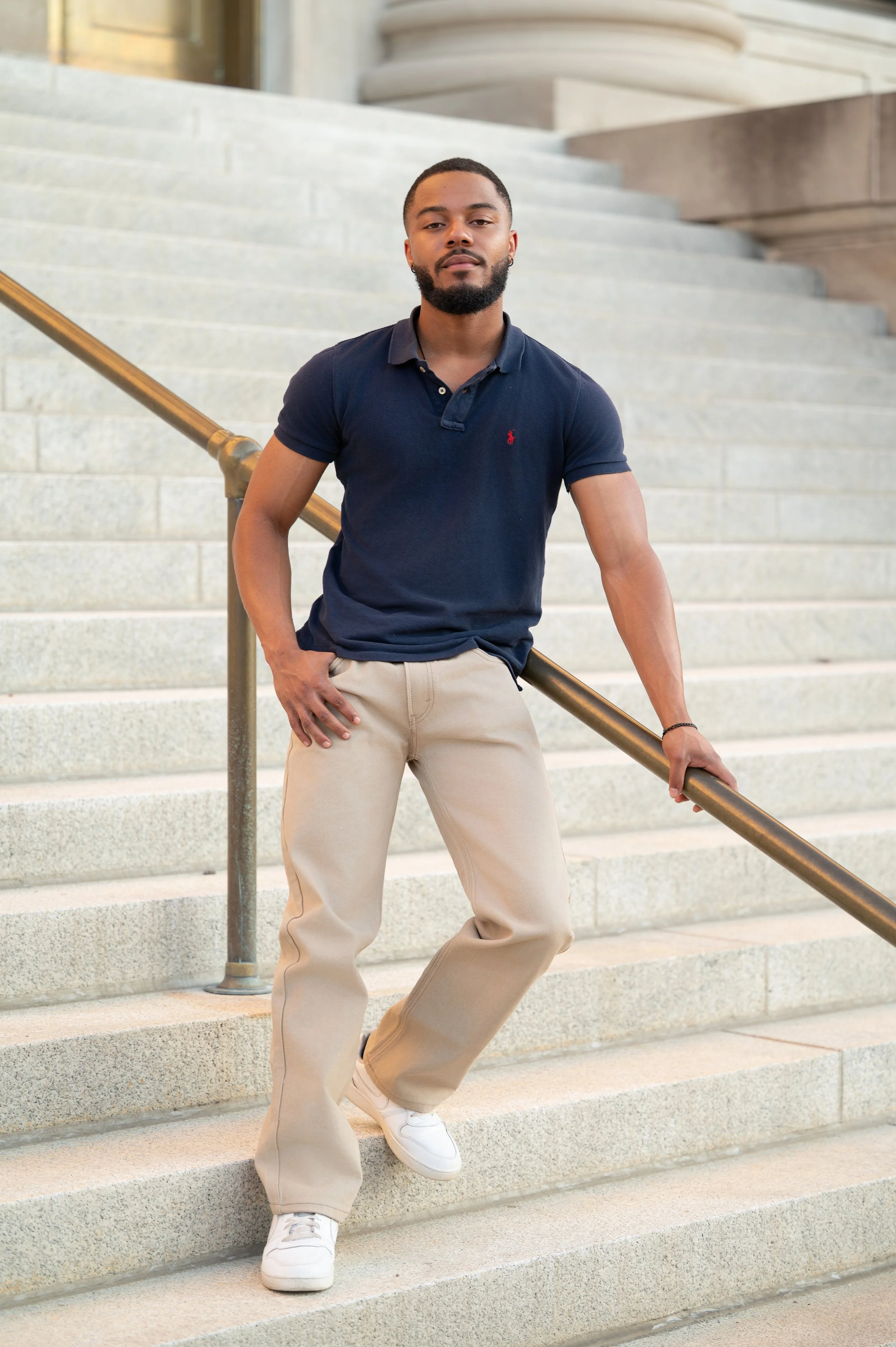 Senior guy in a navy polo leaning against a brass railing on granite courthouse steps