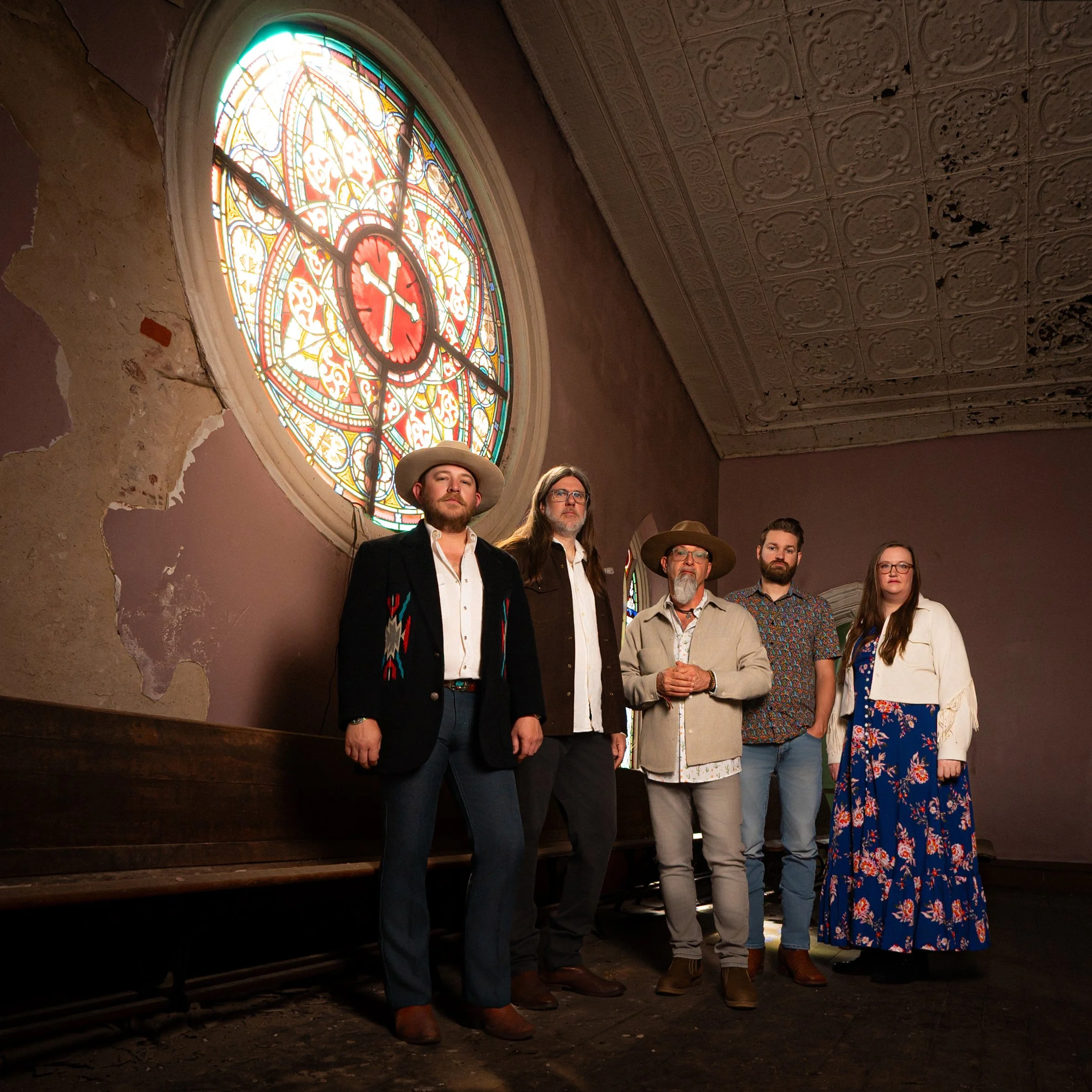 Five-piece band posed beneath a stained-glass rose window in a weathered historic church