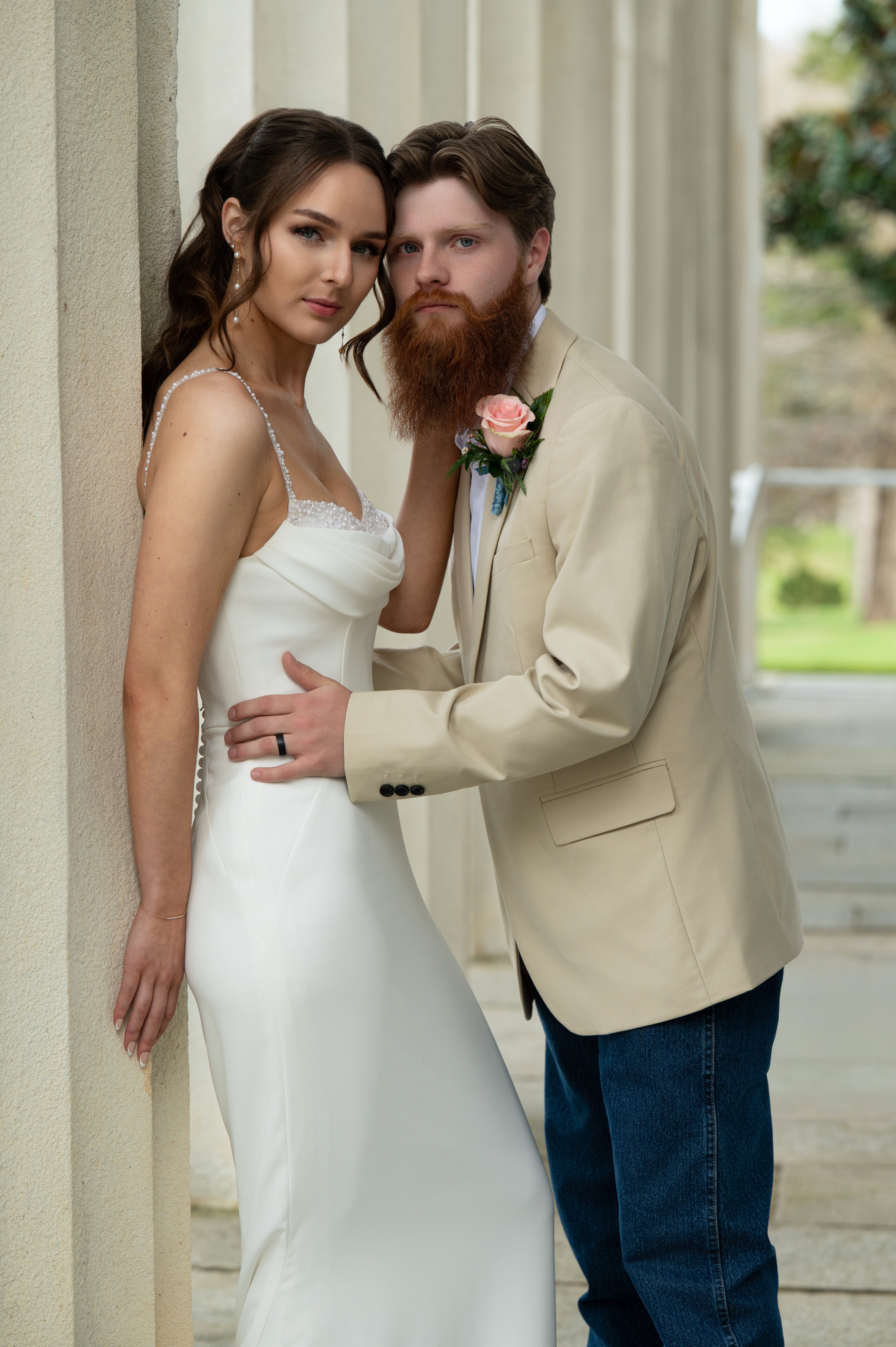 Bride and groom leaning together against tall white columns at Berry Hill, both looking straight down the lens