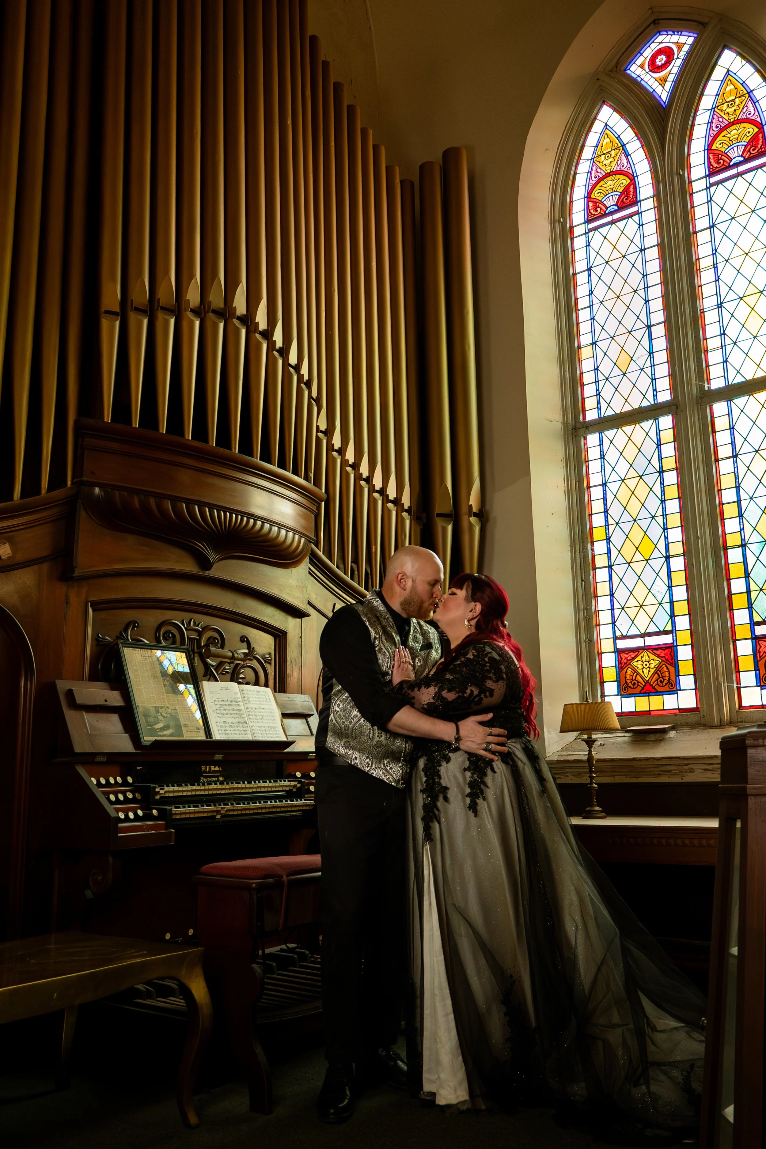 A couple kissing beside the pipe organ beneath a stained-glass window