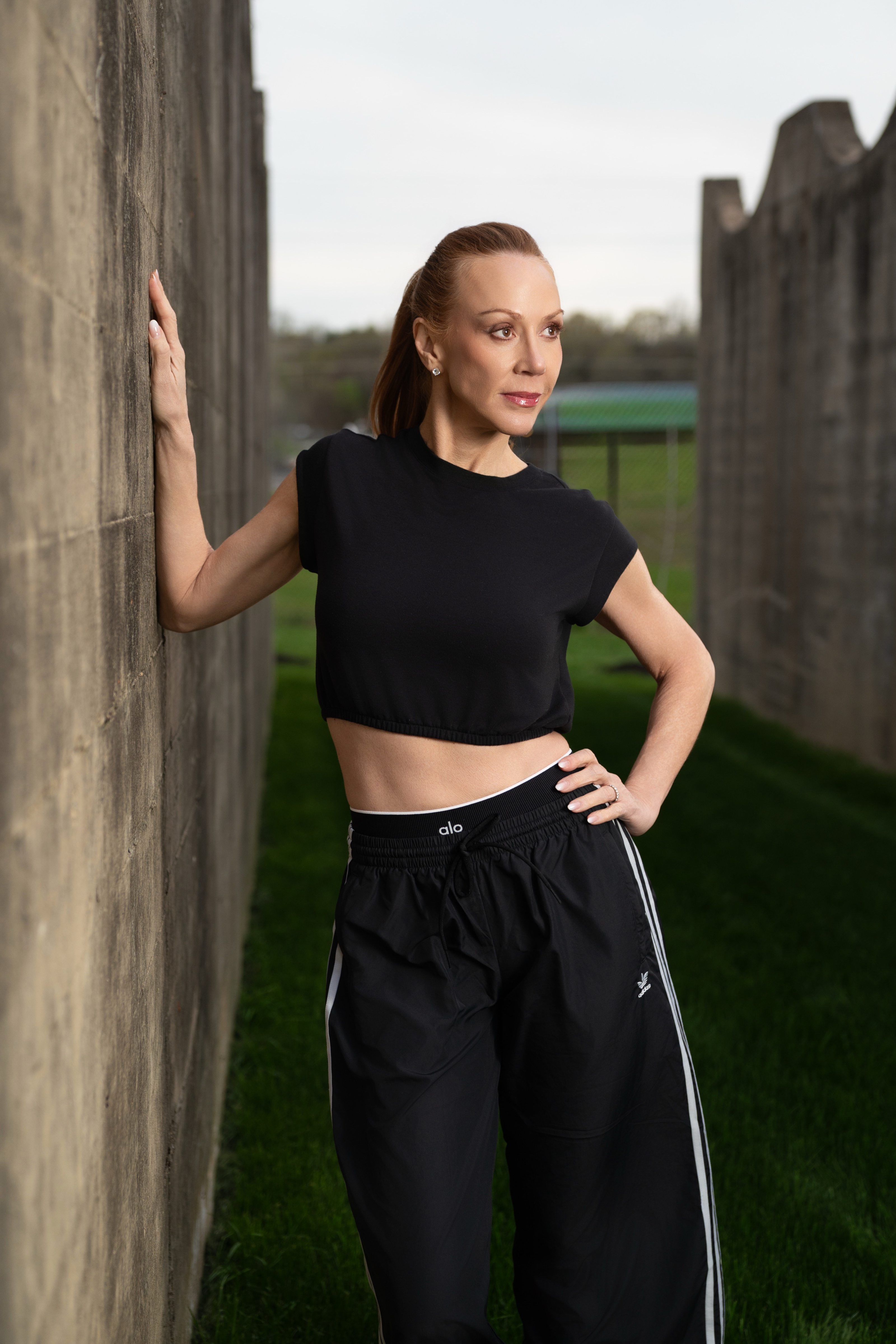 Athlete in a black crop top and track pants posed against a weathered concrete barrier