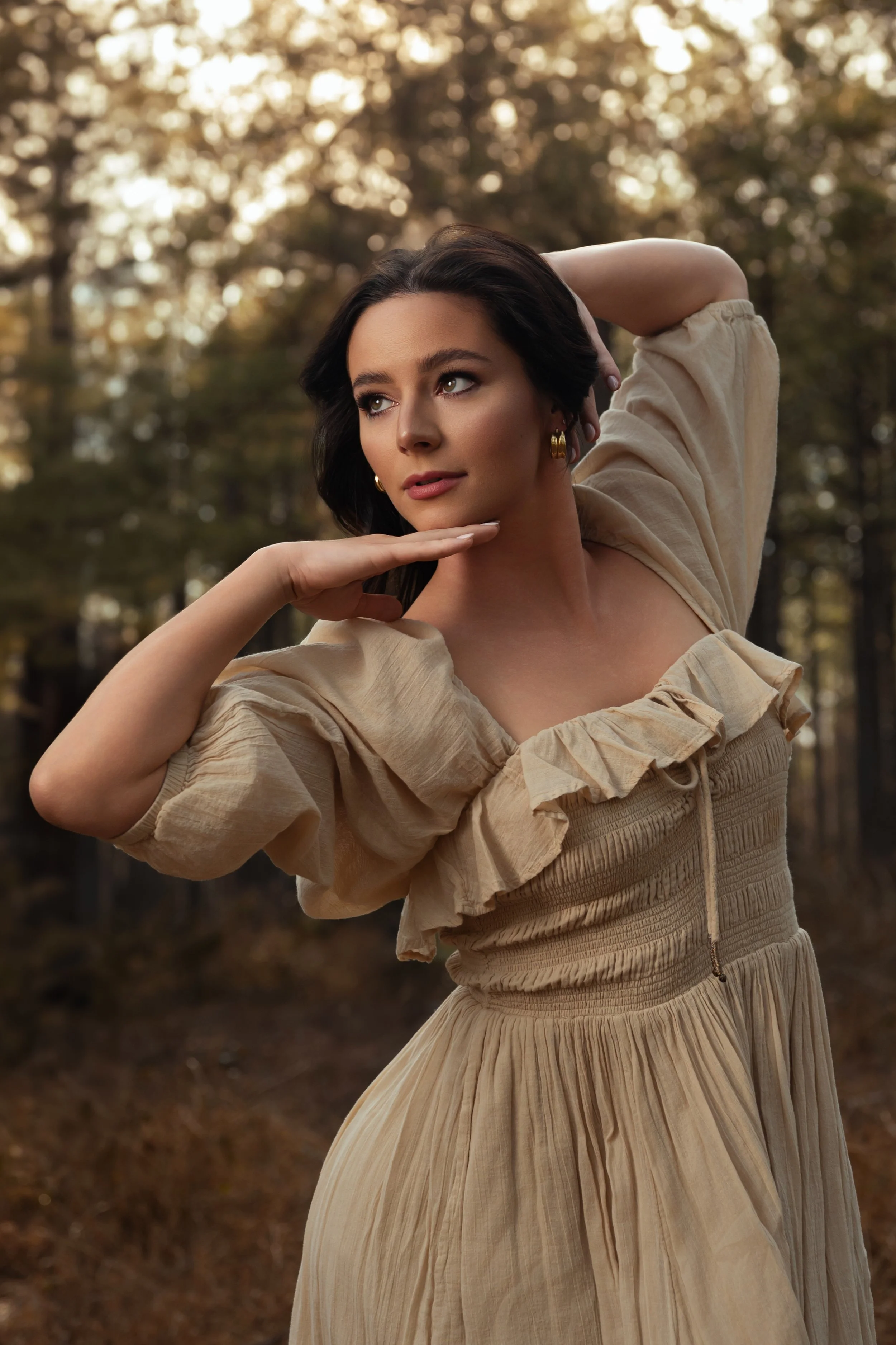 Woman in a cream ruffled dress posing in a sunlit pine forest at golden hour