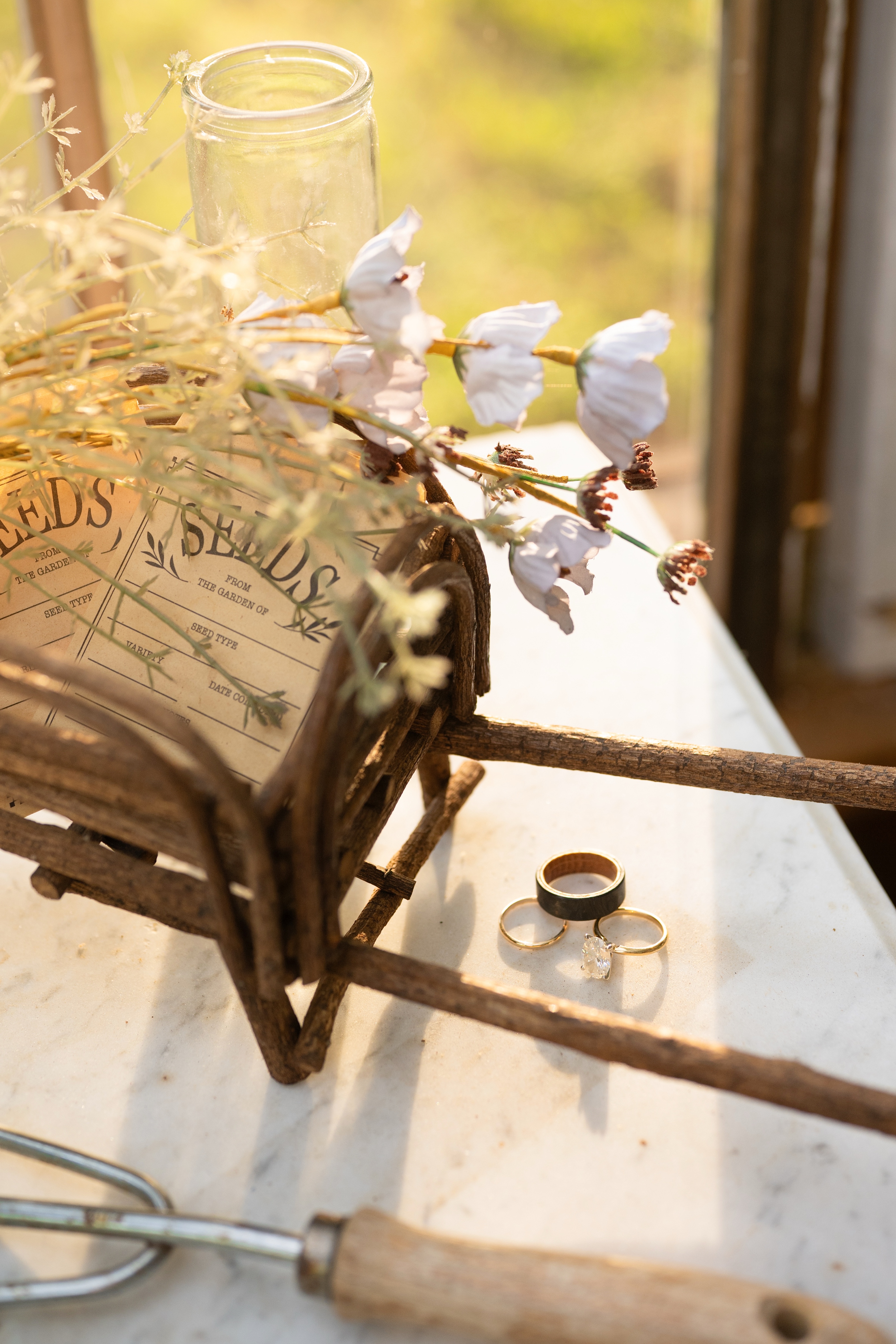 The wedding bands resting on a marble sill beside a rusted garden trug and white blooms