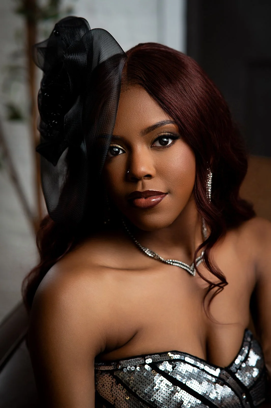 Studio glamour portrait of a senior in a silver sequined dress with a black tulle fascinator