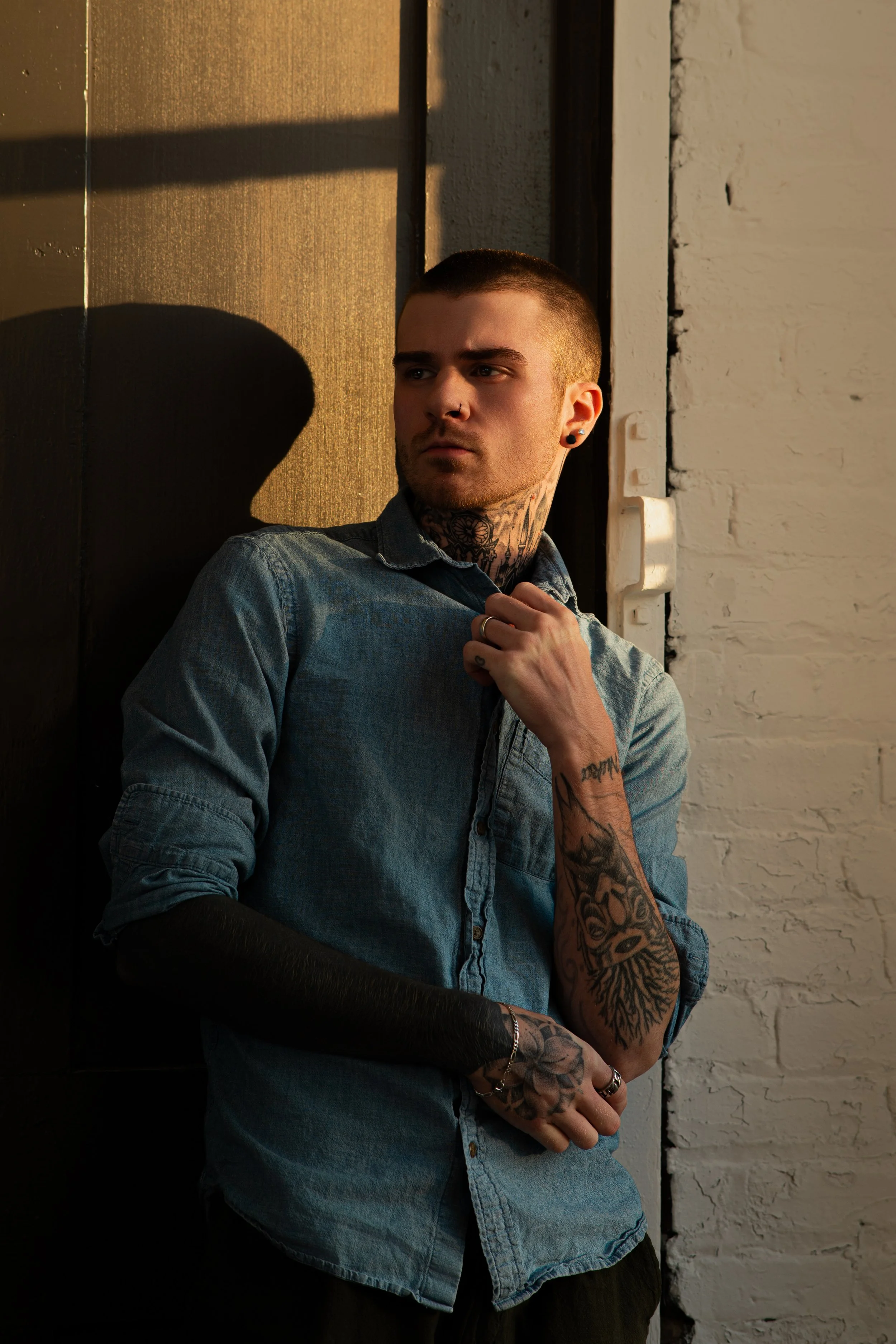 Patrick Gibson, photographer, standing in warm golden-hour light against a white brick wall