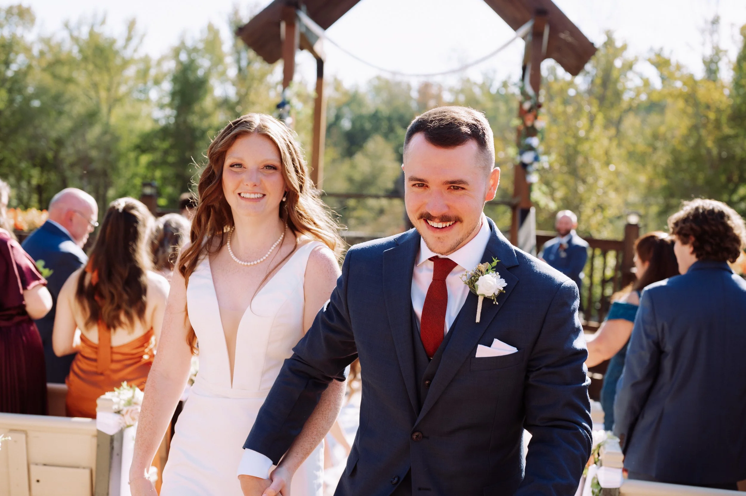 Just-married couple beaming as they walk back up the aisle hand in hand, guests behind them