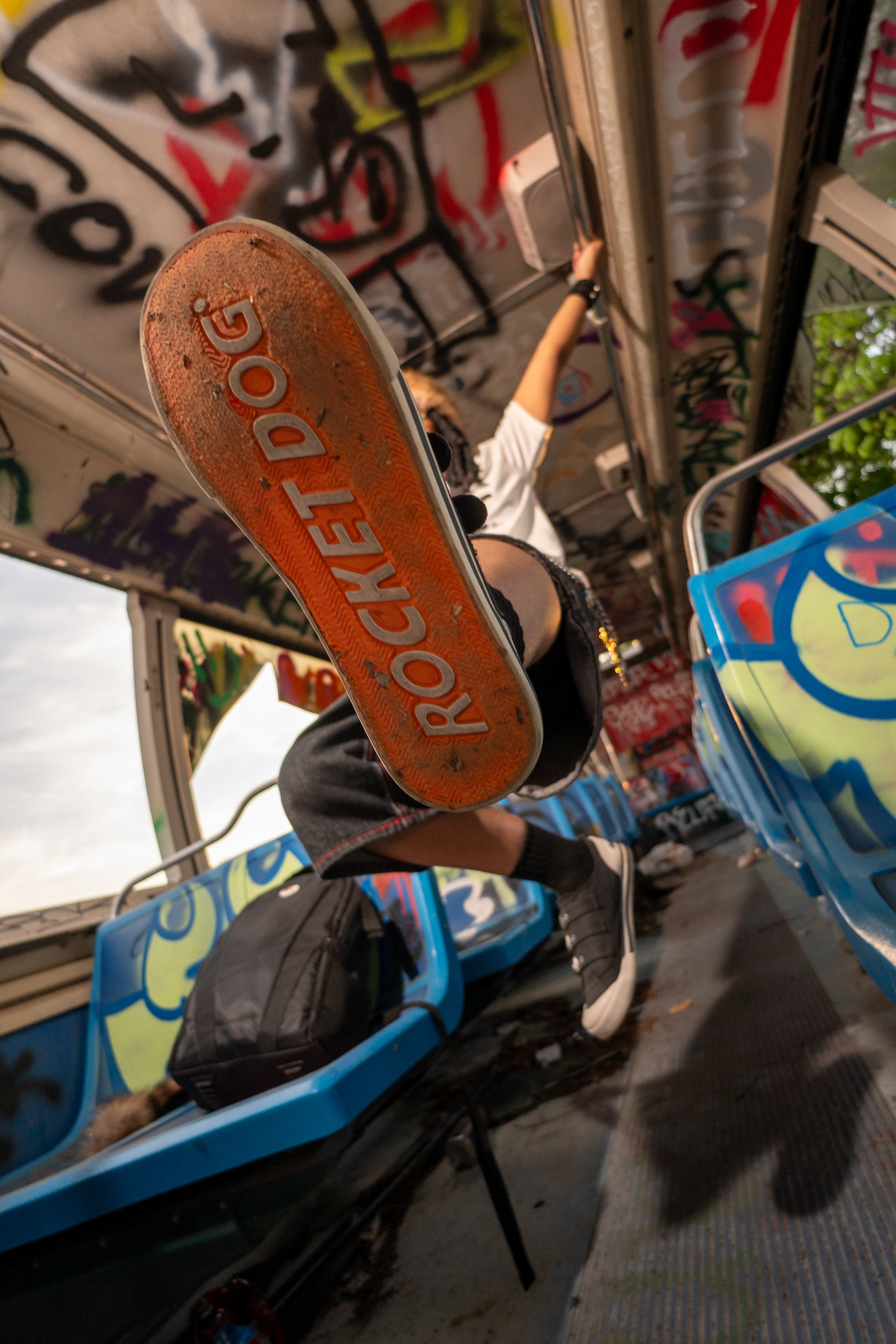 Skater photographed from below mid-air over a graffiti-covered ramp, the board's orange sole filling the frame
