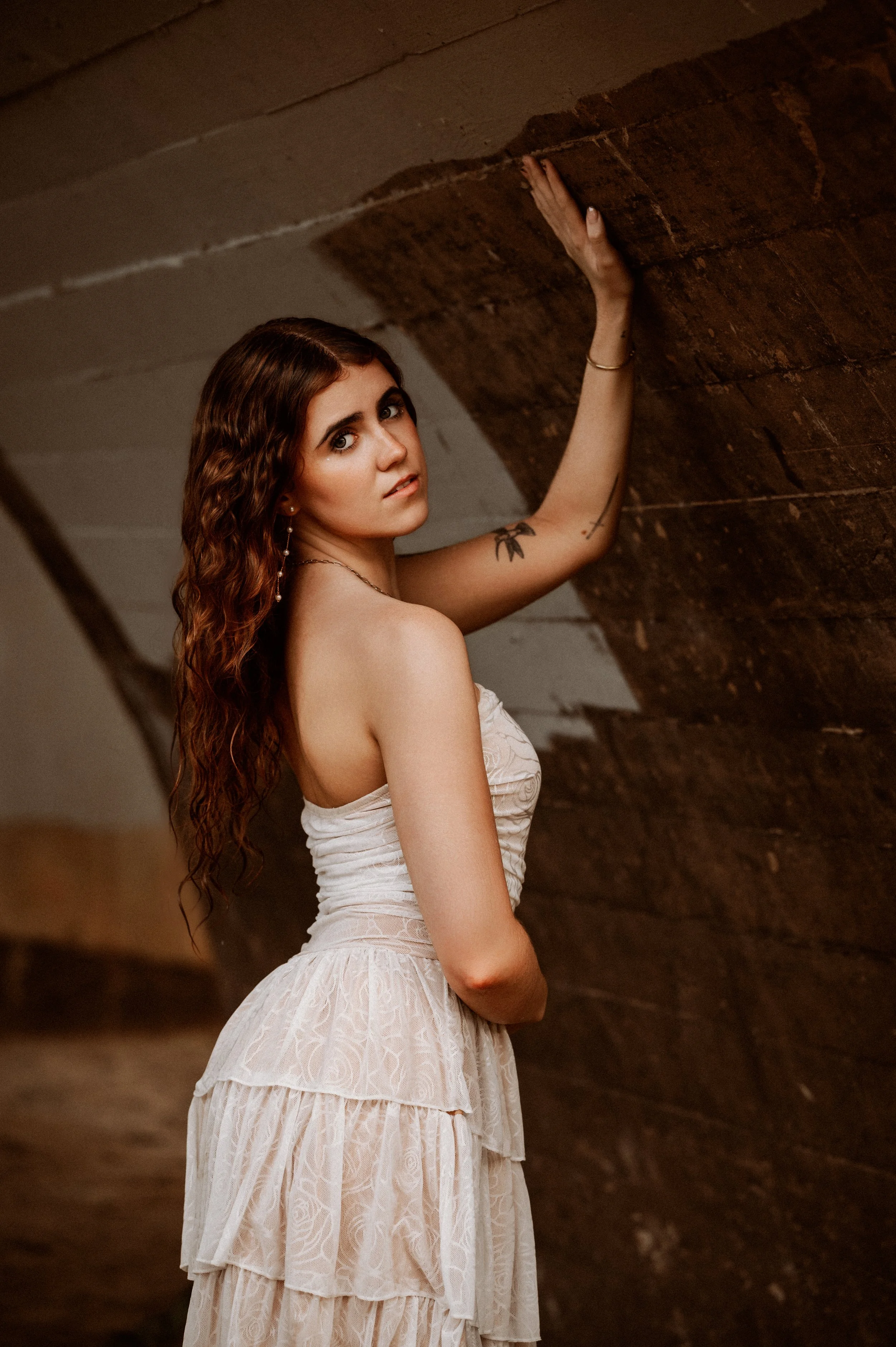 Senior in a tiered white dress glancing over her shoulder beneath a brick-and-concrete arch