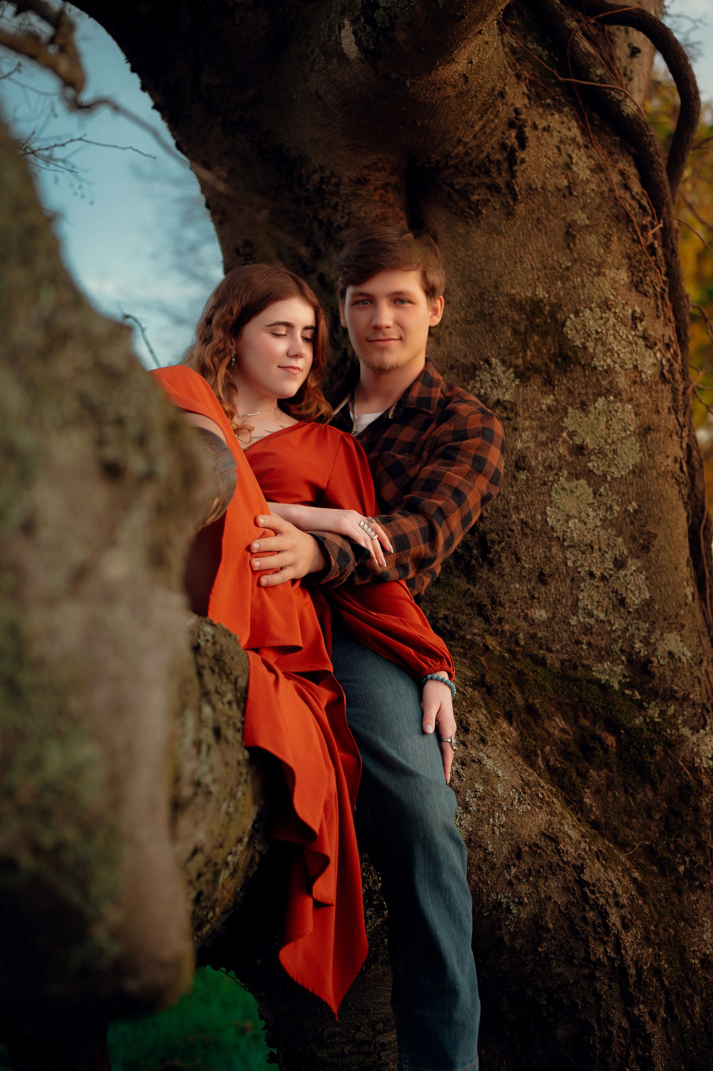 A couple embracing in the hollow of a massive tree, her orange dress bright against the bark