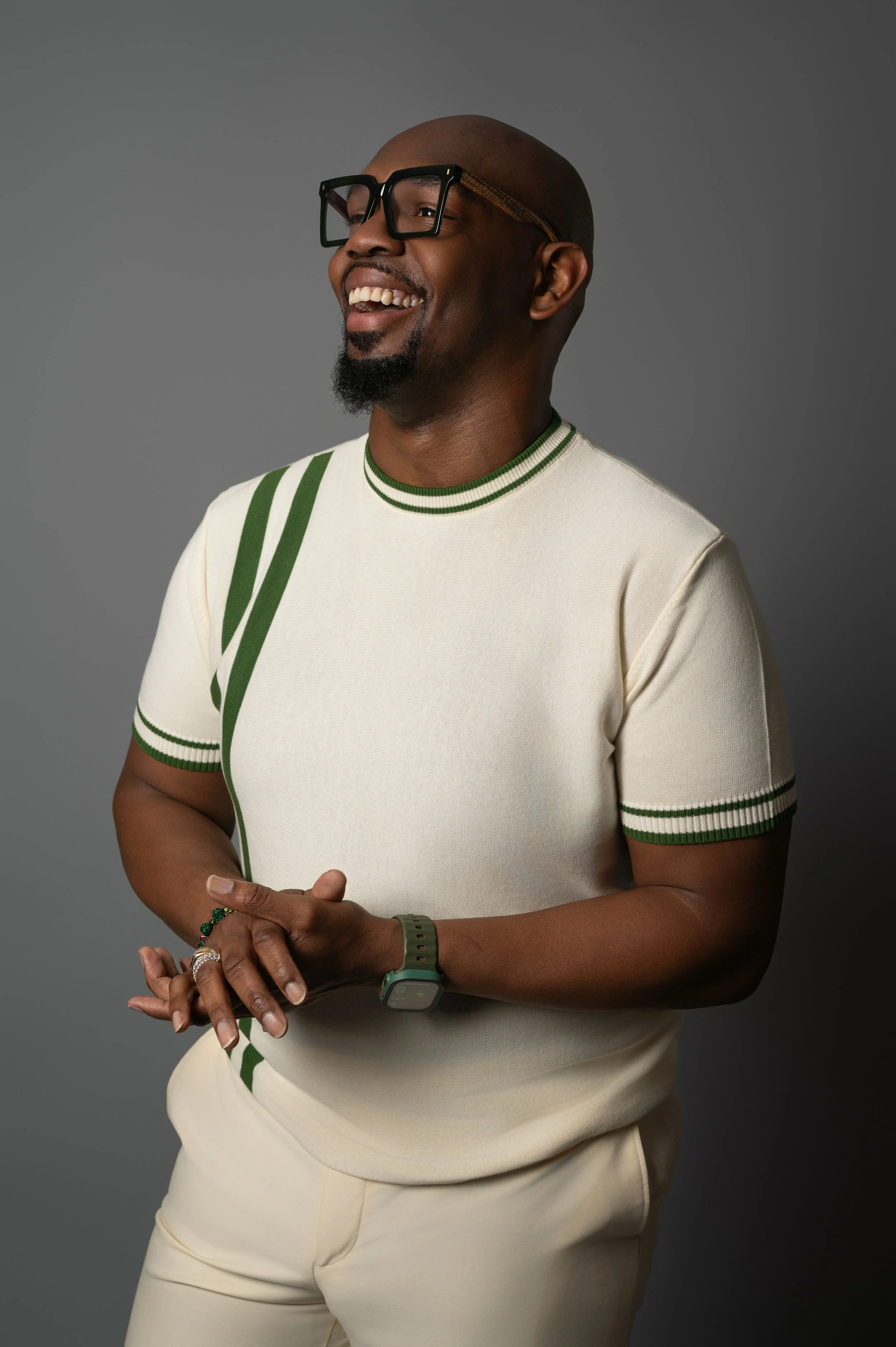 A man in a cream knit set laughing against a grey studio backdrop