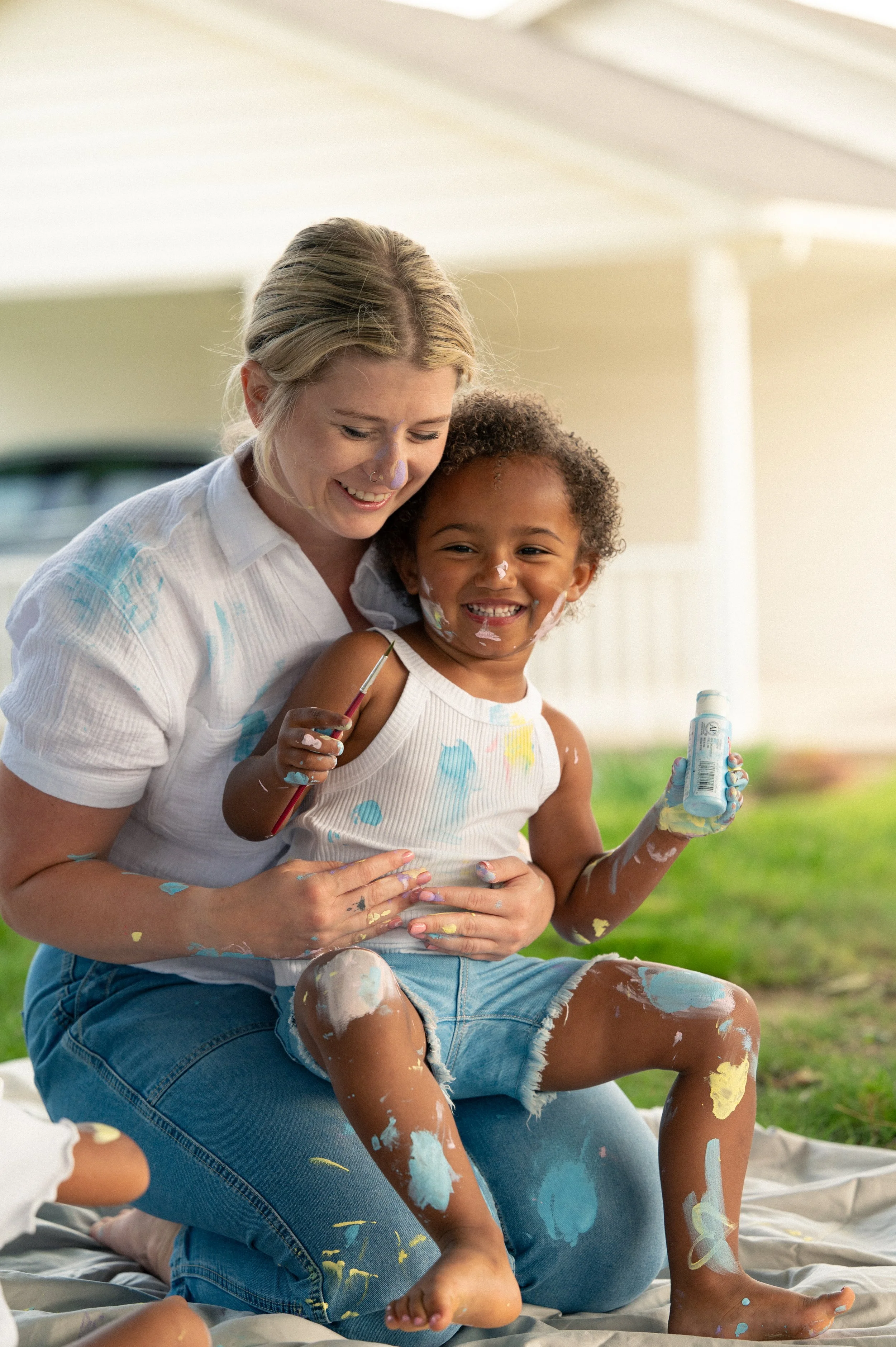 A mother and toddler covered in pastel paint, laughing together on a drop cloth