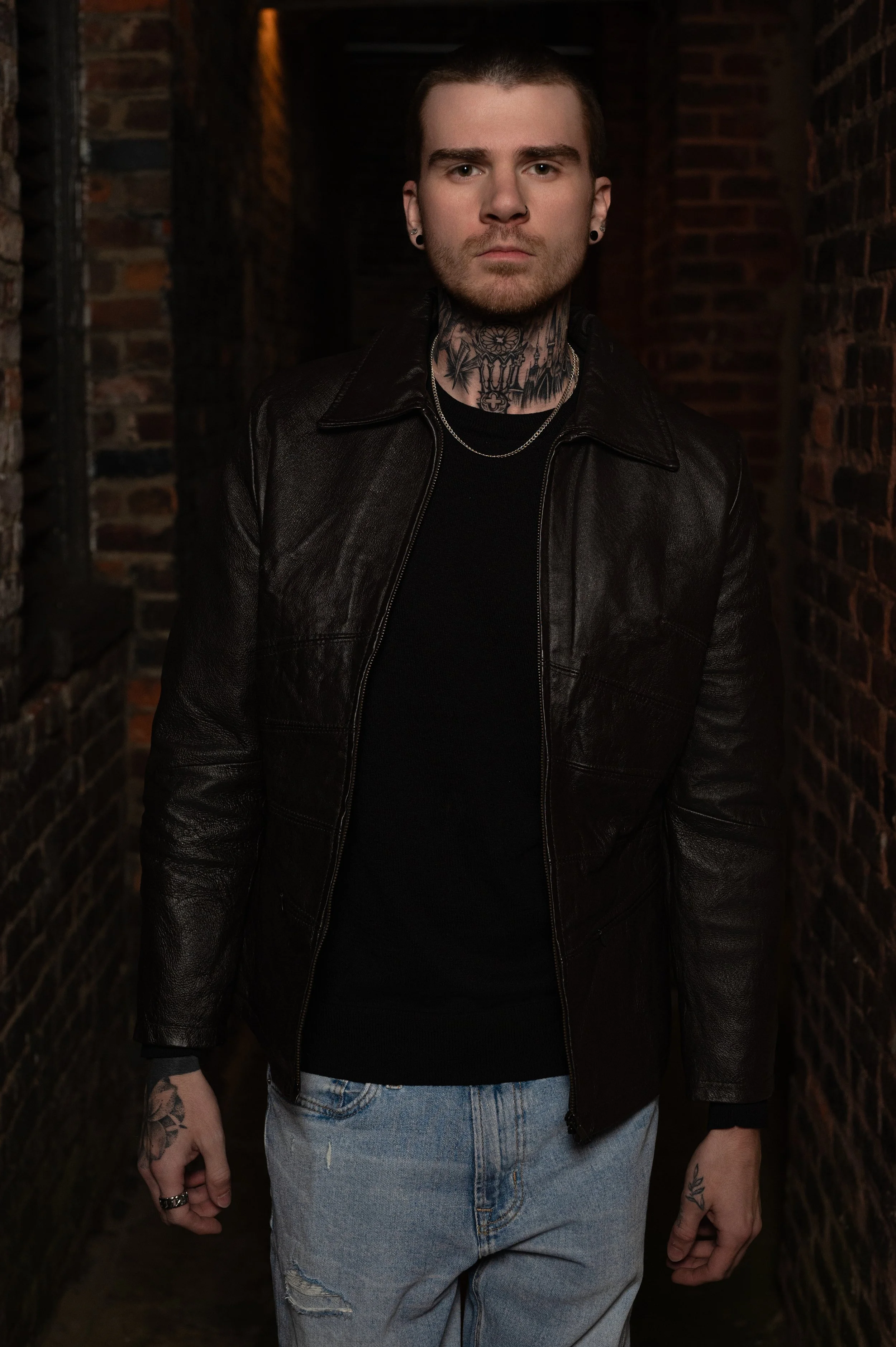 Patrick Gibson standing in a narrow brick alleyway in a leather jacket — the warehouse-district brick of Danville, Virginia