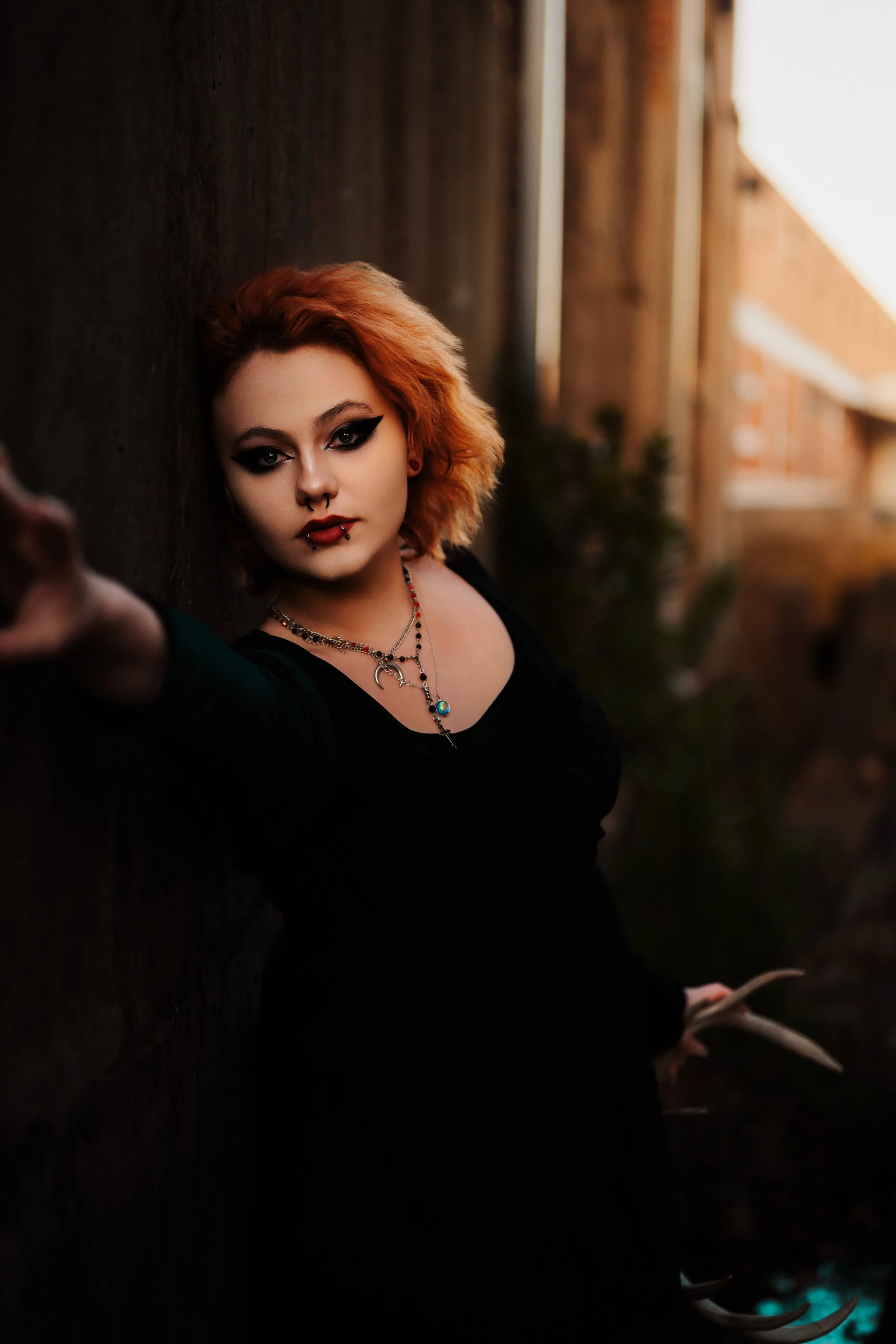 Senior with copper hair and bold winged eyeliner in a black dress, posed against warehouse-district brick