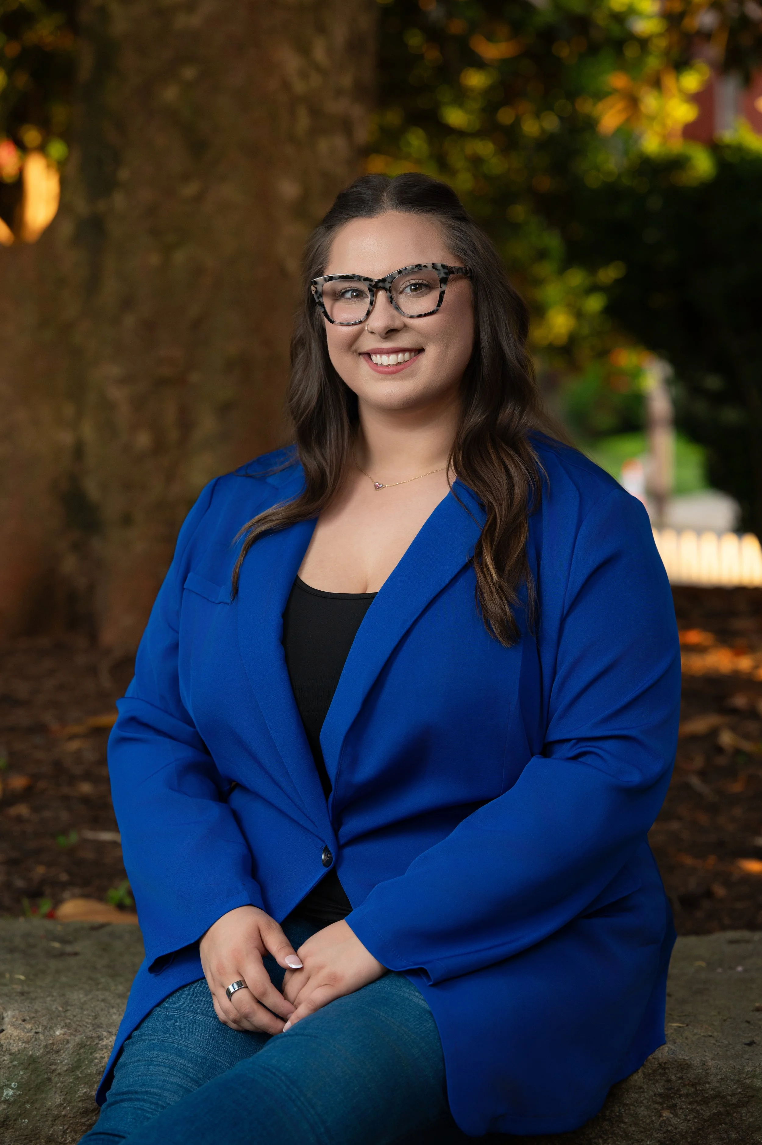 Woman in a cobalt blazer and patterned glasses smiling under a magnolia tree