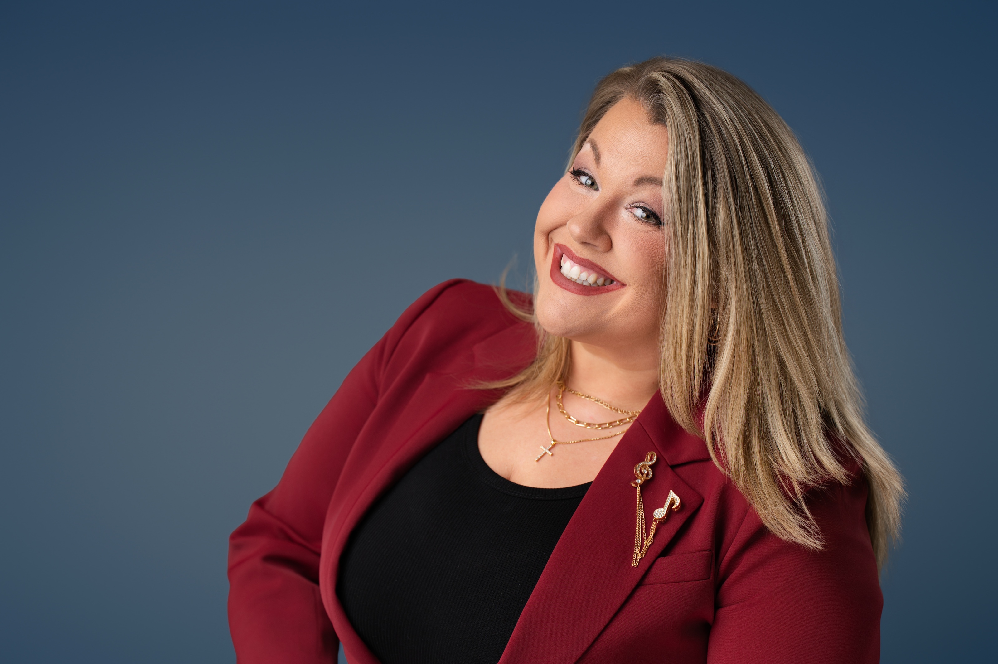 Studio headshot of a smiling woman in a red blazer against a deep blue backdrop