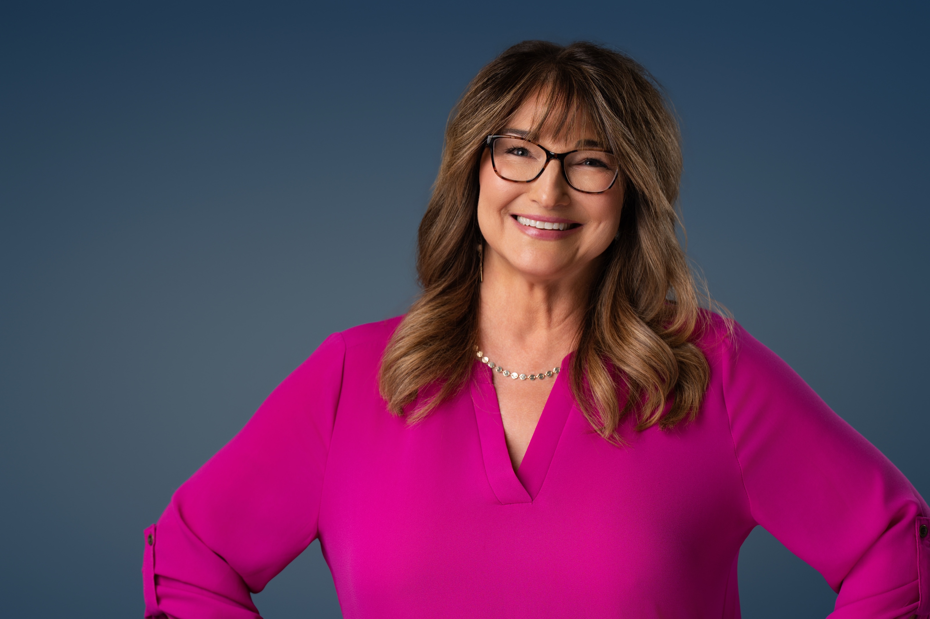 Studio headshot of a woman in a magenta top and glasses against a deep blue backdrop