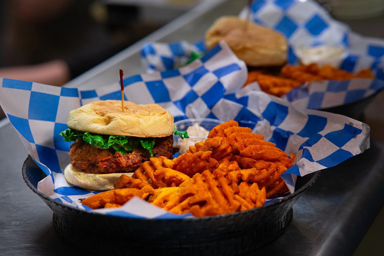 A crispy fried chicken sandwich with lettuce and a basket of sweet potato waffle fries, photographed for a restaurant