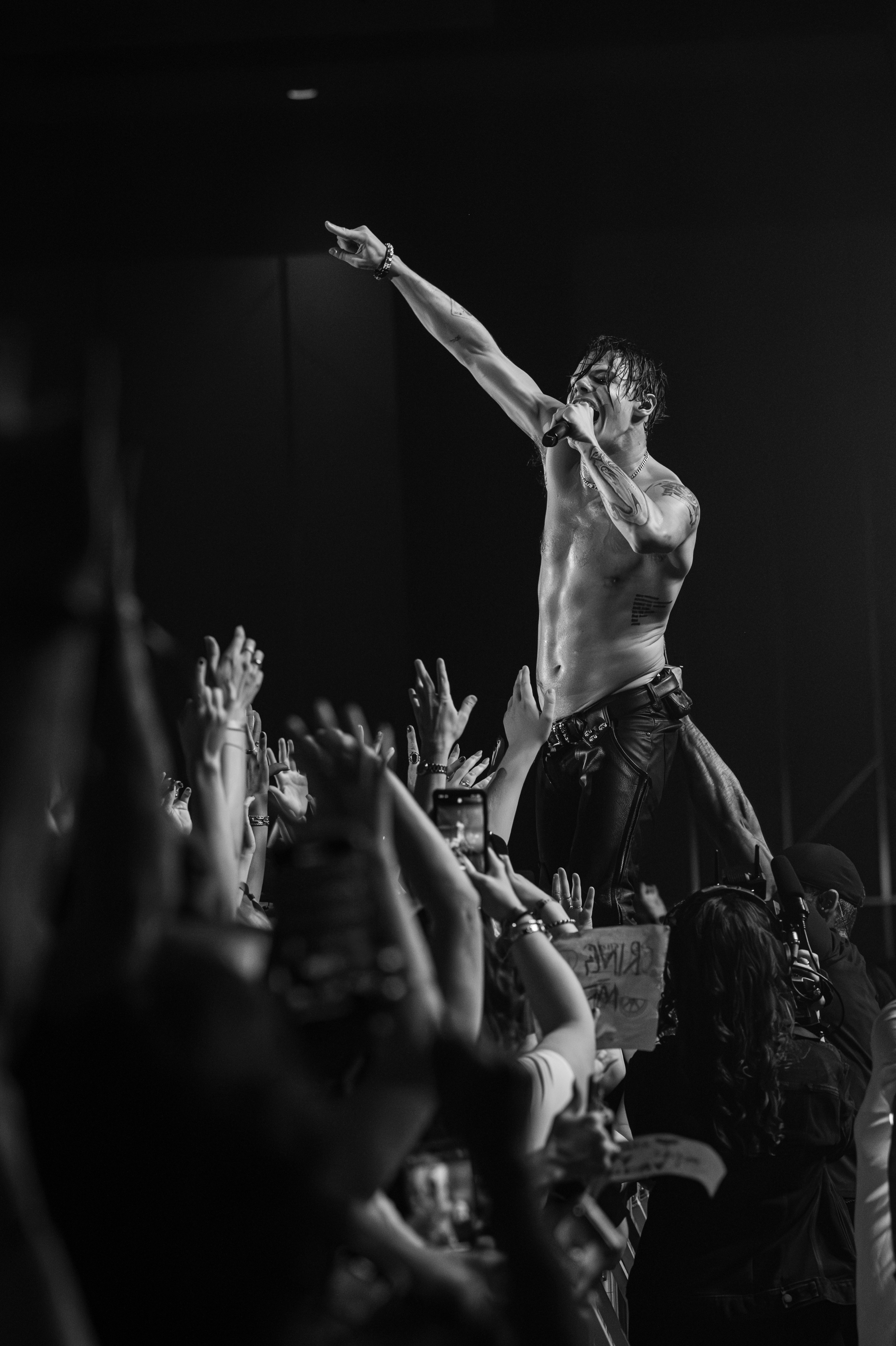 Black-and-white frame of a shirtless singer reaching out over a sea of raised hands at the barricade