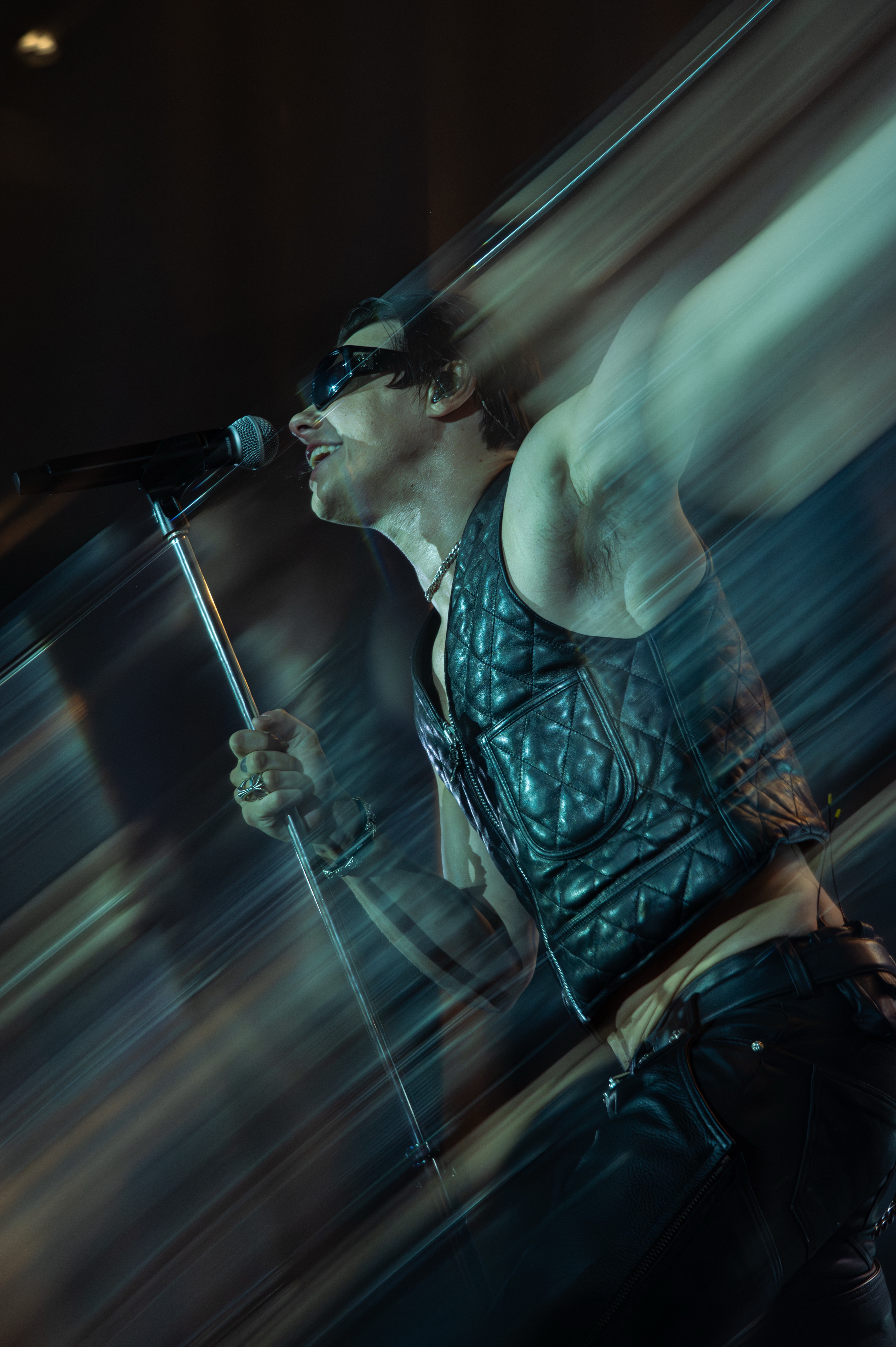 A singer leaning back into the microphone stand, captured with a sweeping motion blur under blue stage light
